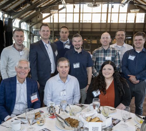 Aeon Affordable Homes A group of ten people pose and smile at a banquet table during an indoor event or conference.