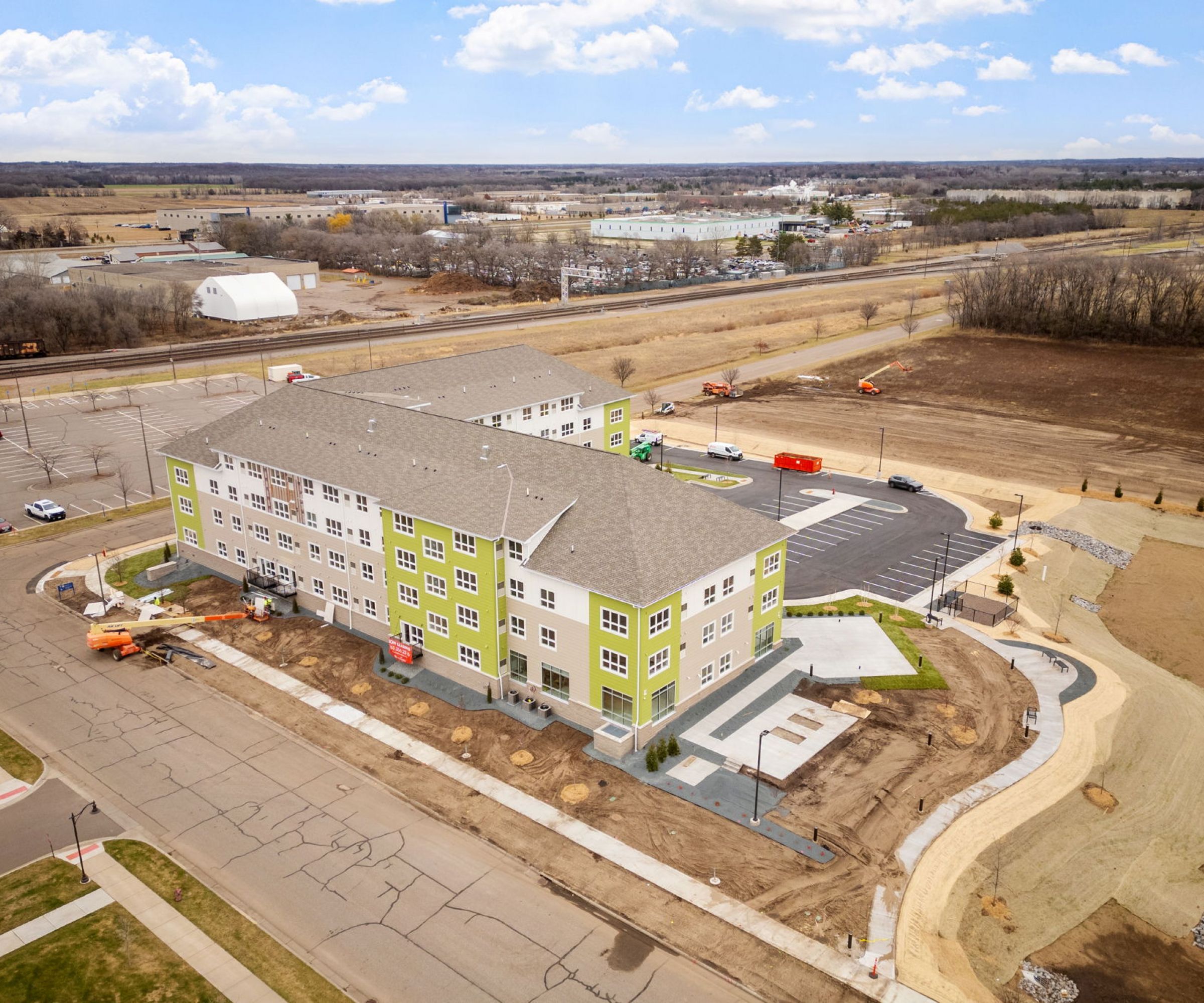 Aeon Affordable Homes and Community Aerial view of an affordable apartment home, a new light green four-story building with a parking lot and surrounding roads on a clear day.