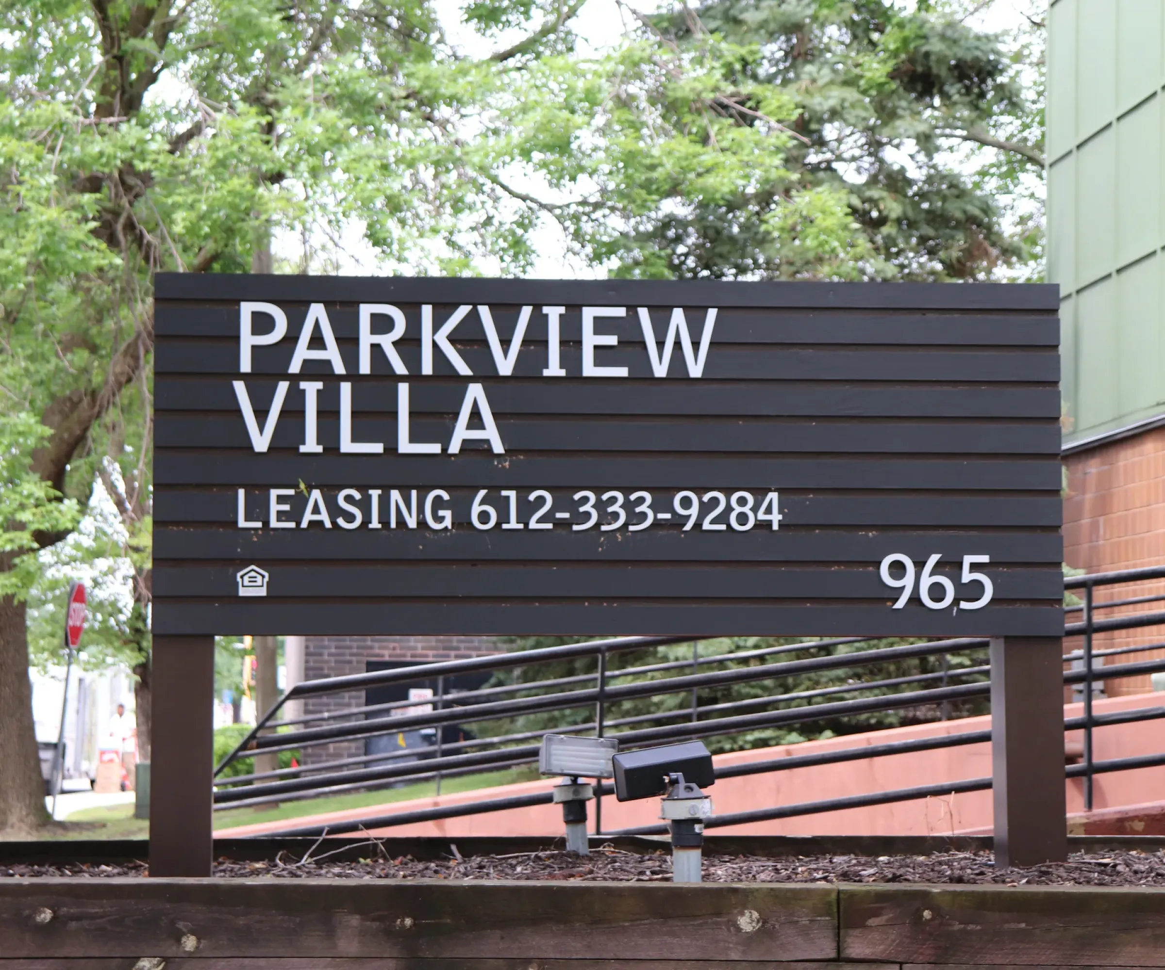 Aeon Affordable Homes and Community Sign reading "Parkview Villa Leasing 612-333-9284," number 965, surrounded by trees and a building offering affordable apartment homes.