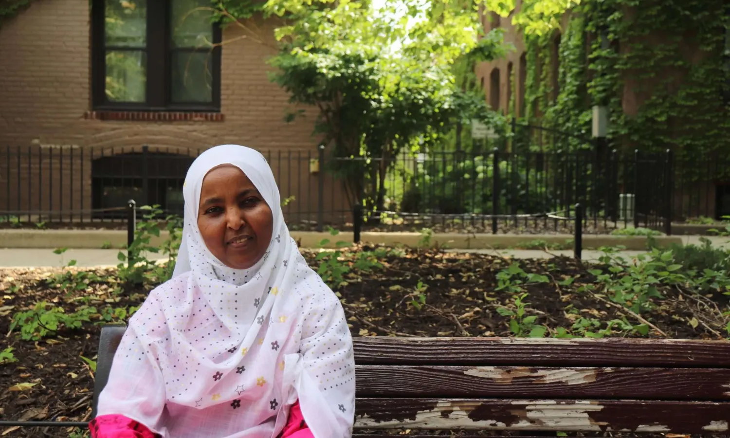 Aeon Affordable Homes with a resident sitting on a bench outside of an apartment community and smiling