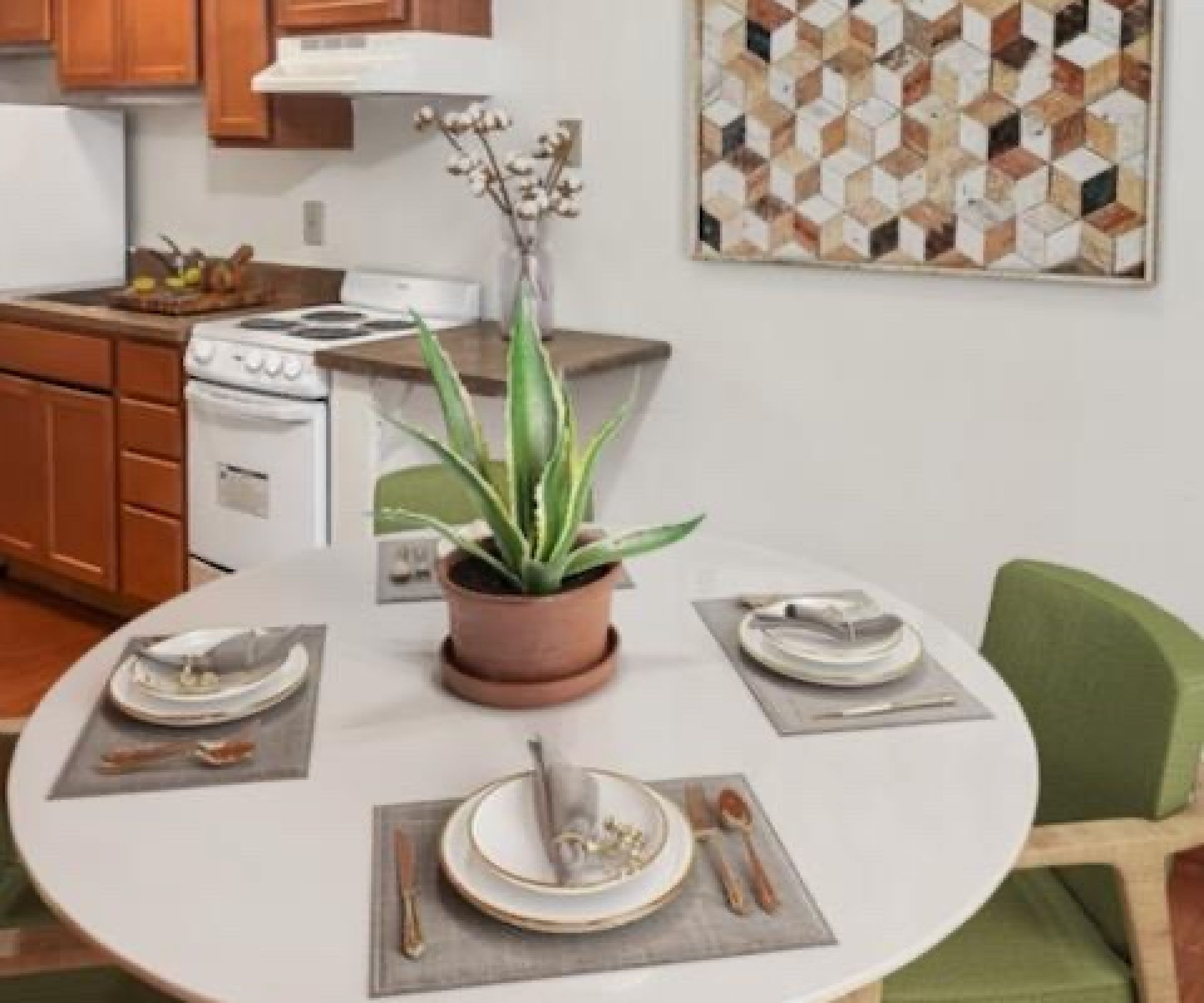 Aeon Affordable Homes and Community Dining area in affordable apartment homes: a round table for four, green chairs, plant centerpiece, and geometric art adorn the walls.