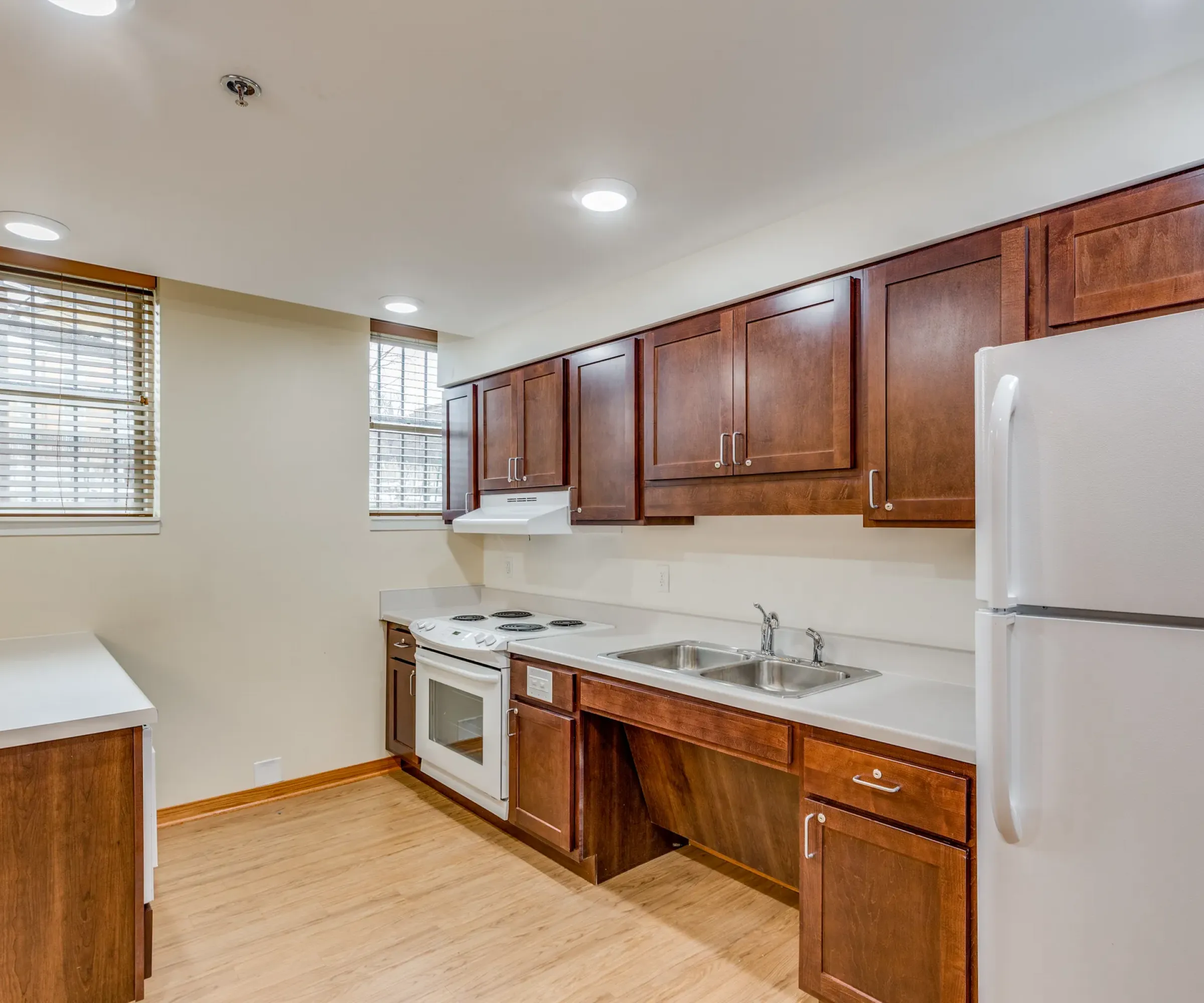 Aeon Affordable Homes and Community Modern kitchen in affordable apartment homes with wooden cabinets, white countertops, stove, sink, and a refrigerator. Natural light floods in.