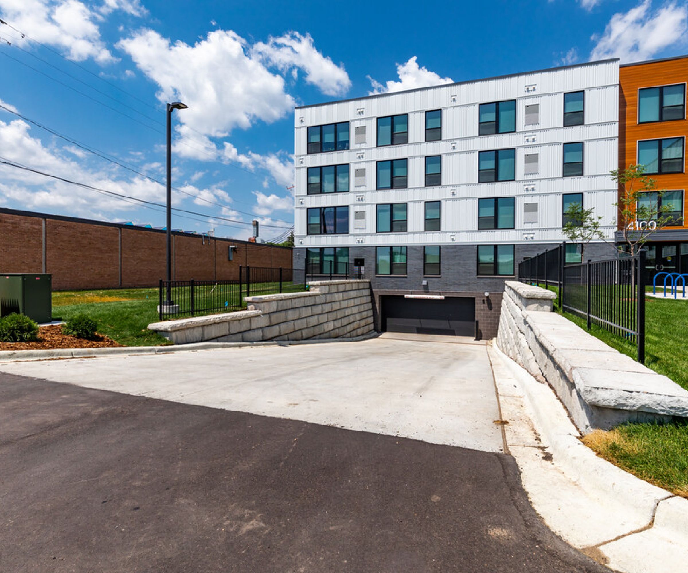 Aeon Affordable Homes and Community Entrance to an underground parking garage beside a modern building offering affordable apartment homes under a partly cloudy sky.