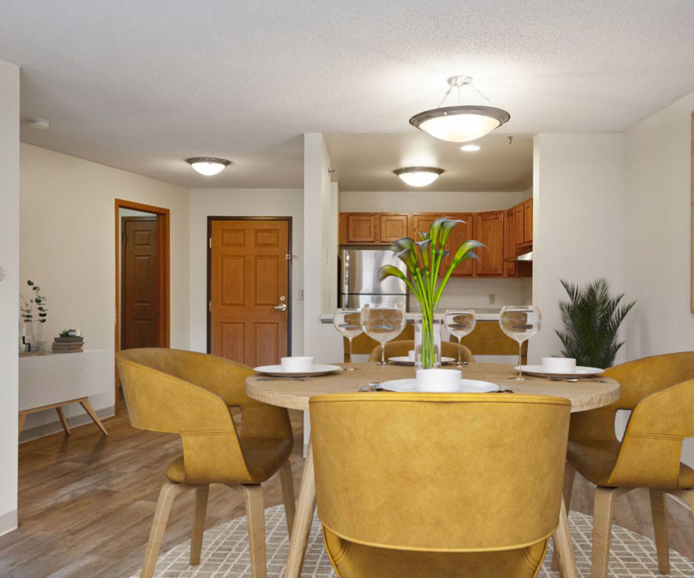 Aeon Affordable Homes and Community A dining area with a round wooden table, yellow chairs, and a modern kitchen in the background showcases stylish affordable apartment homes.