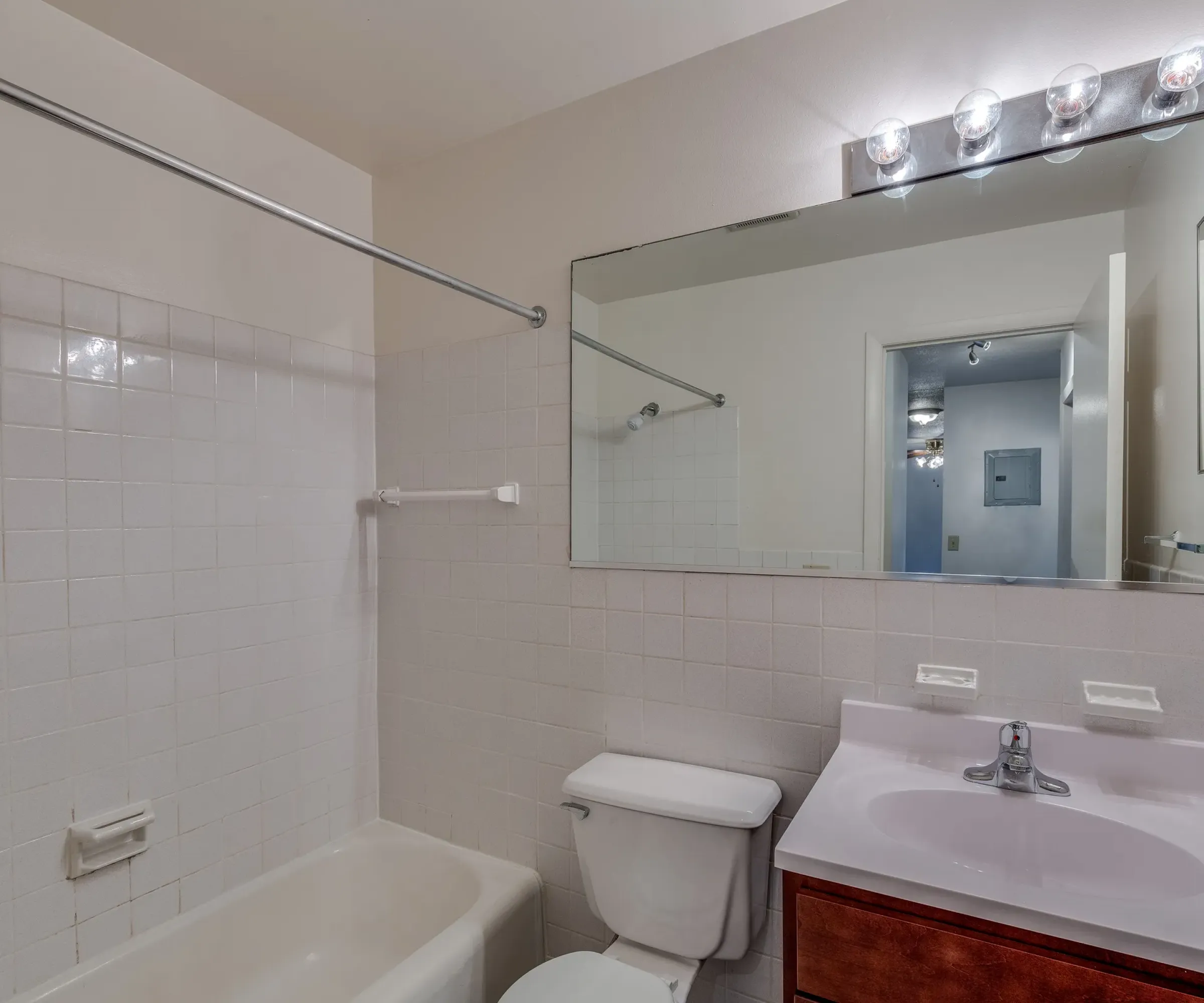Aeon Affordable Homes and Community Affordable apartment homes feature a bathroom with a tub, toilet, and vanity, accented by white tiles and neutral colors for a serene space.