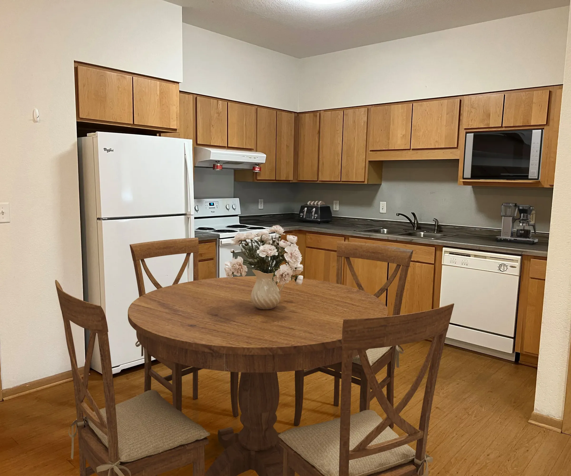 Aeon Affordable Homes and Community A cozy kitchen in affordable apartment homes with wooden cabinets, a round dining table, chairs, and essential appliances for convenience.