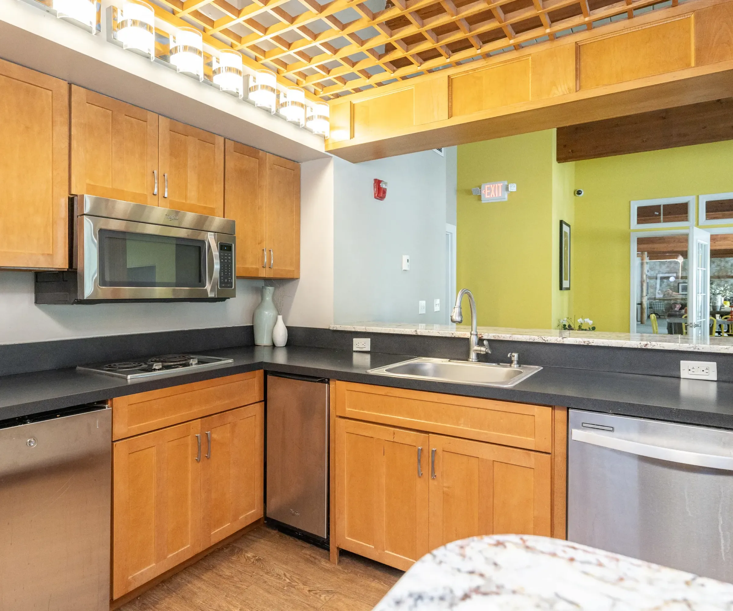 Aeon Affordable Homes Modern kitchen with wooden cabinets, stainless steel appliances, black countertops, and a mirrored wall, embodying Blooming Meadows elegance.