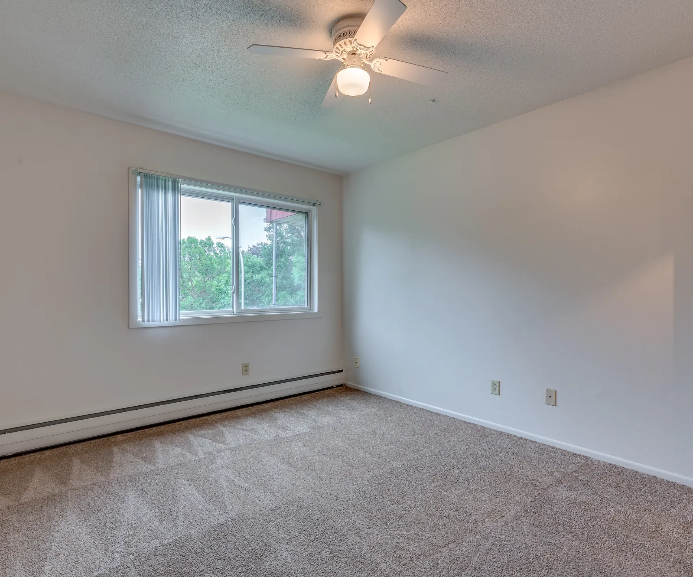 Aeon Affordable Homes and Community An affordable apartment home featuring an empty room with beige carpet, a ceiling fan, large window, and white walls.