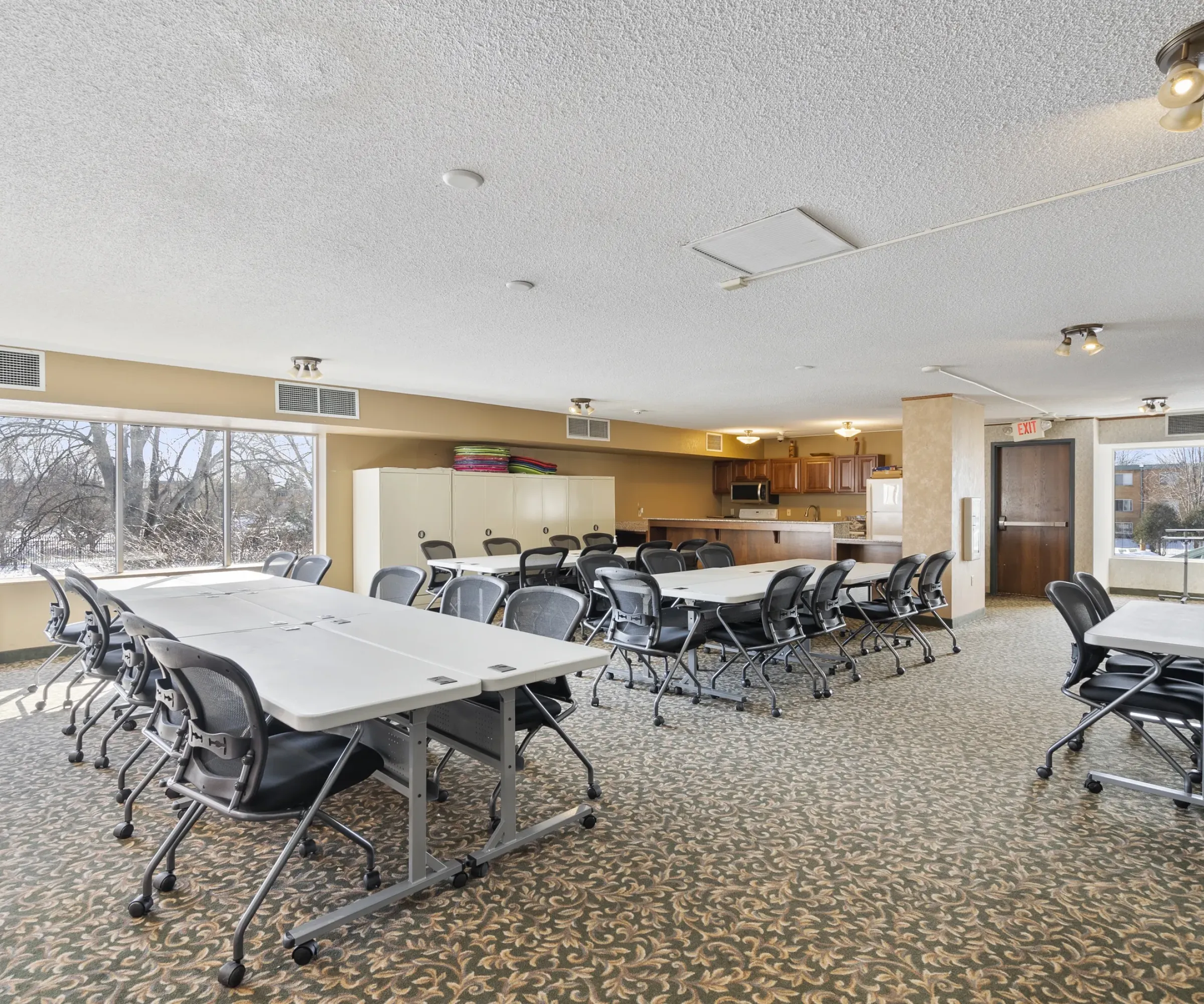 Aeon Affordable Homes Conference room with chairs around tables, large windows, carpeted floor, and a small kitchen area in the back.