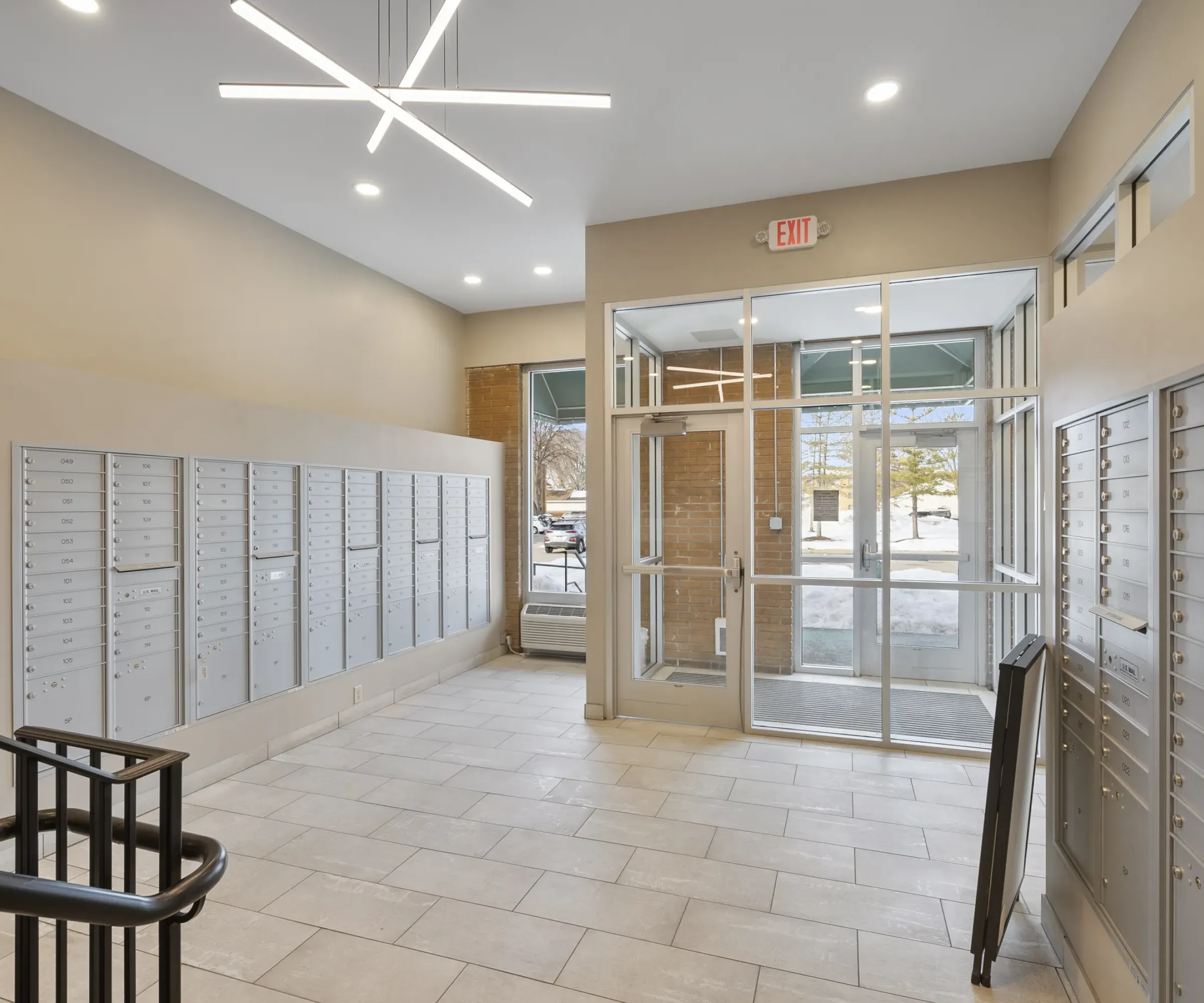 Aeon Affordable Homes Apartment mailroom with mailboxes, modern lighting, glass doors, and outside view on a snowy day.