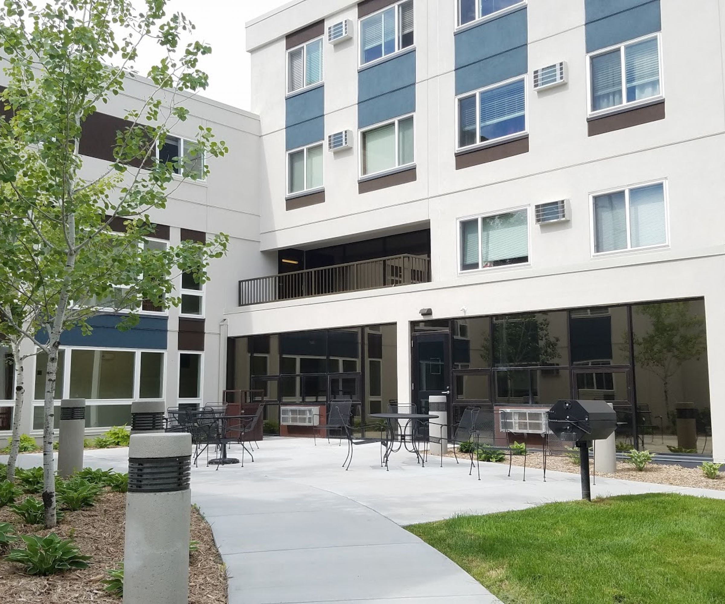 Aeon Affordable Homes and Community Modern, affordable apartment homes with a courtyard, young trees, and inviting outdoor seating areas.