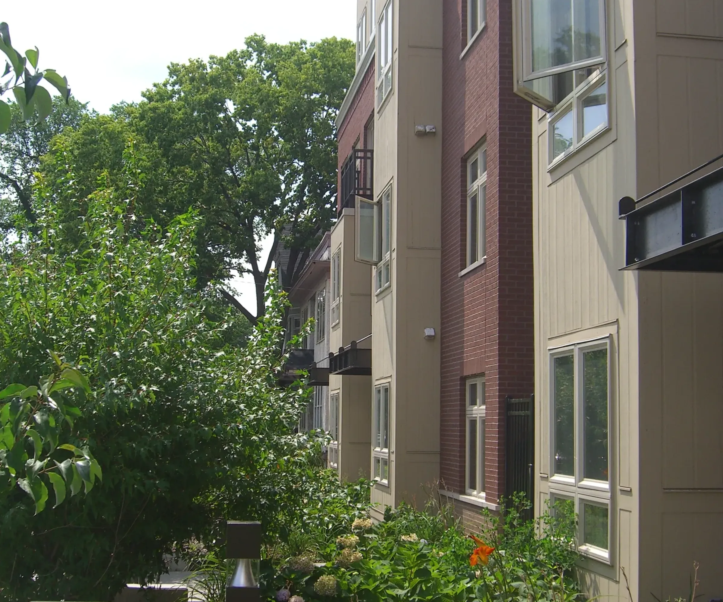 Aeon Affordable Homes and Community Modern apartment building with brick and beige siding, offering affordable apartment homes, surrounded by lush greenery and trees.