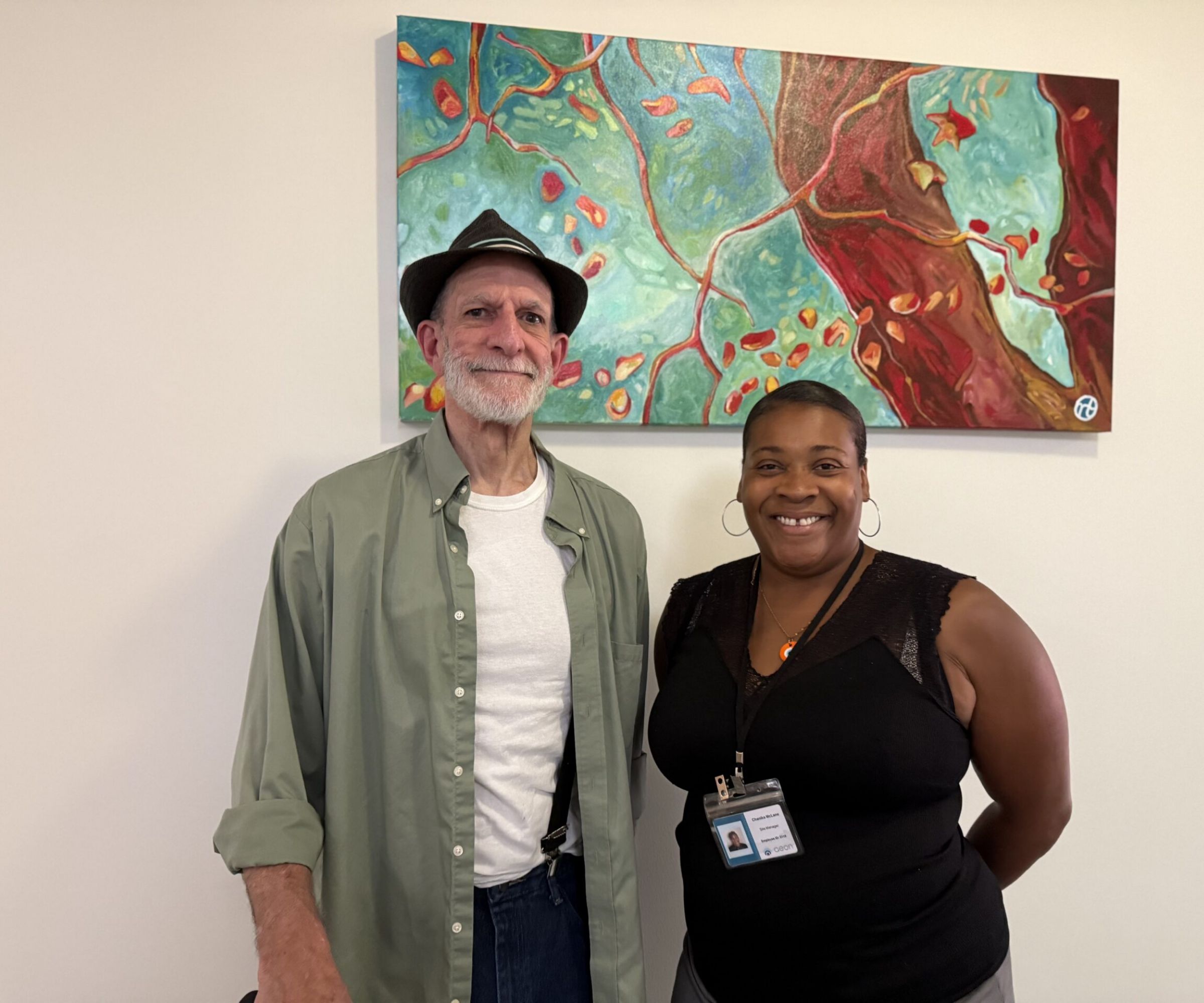 Aeon Affordable Homes Two people smiling and standing in front of a colorful abstract painting on a wall.