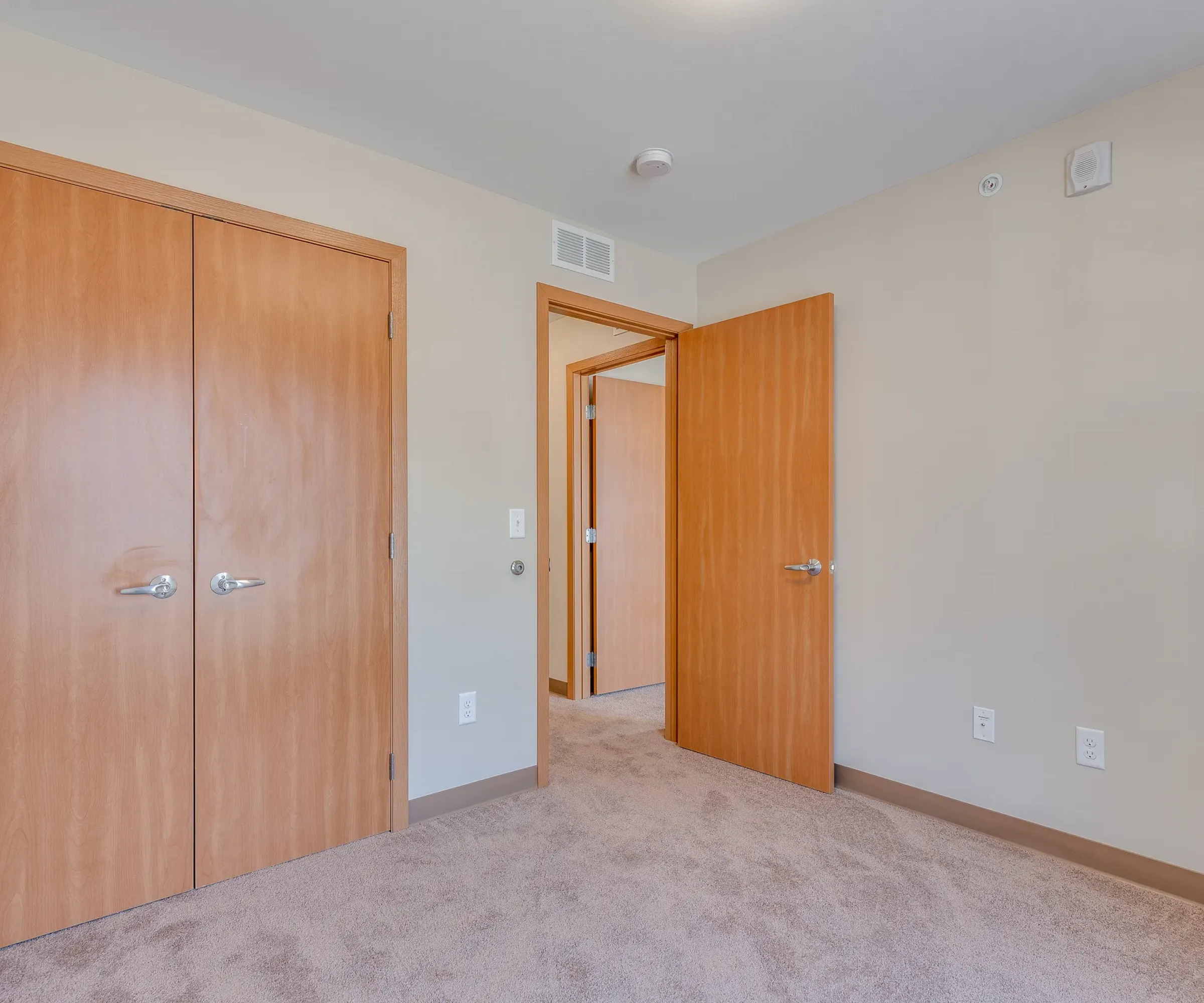 Aeon Affordable Homes and Community Affordable apartment homes featuring empty rooms with beige carpet, light wood doors opening to another room, and neutral walls.