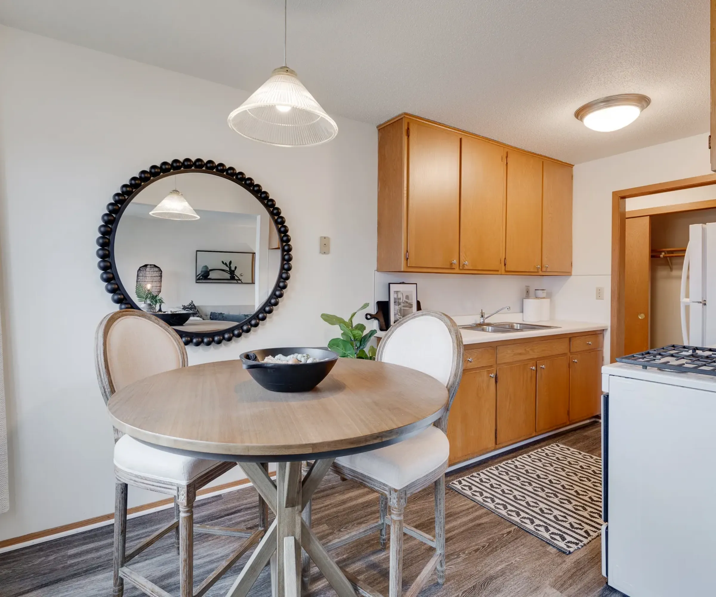 Aeon Affordable Homes A cozy kitchen with a round table, four chairs, wall mirror, wooden cabinets, and a stove near the refrigerator.
