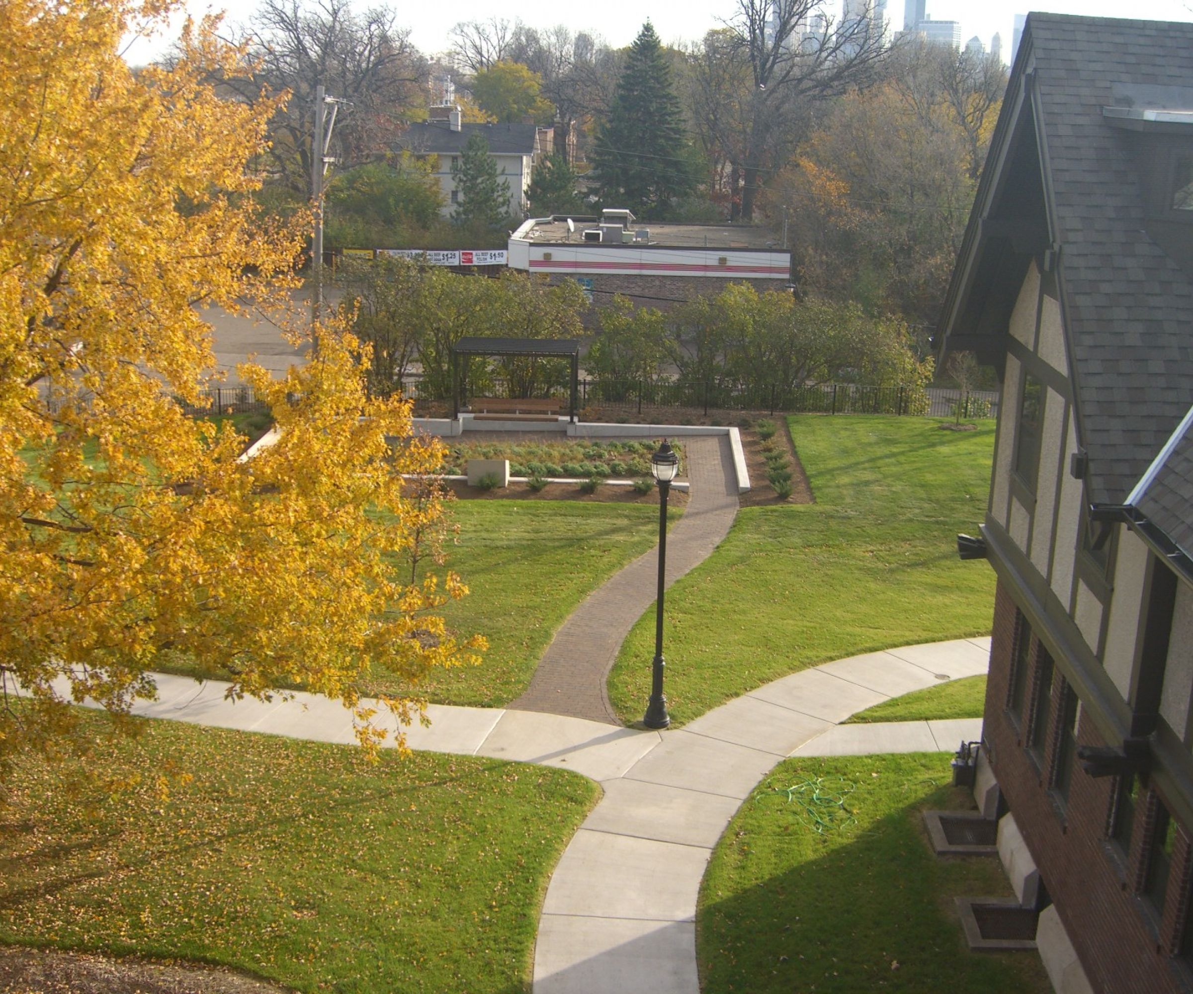 Aeon Affordable Homes and Community Aerial view of a park with autumn trees, pathways, and a pavilion near affordable apartment homes and a large Tudor-style building.
