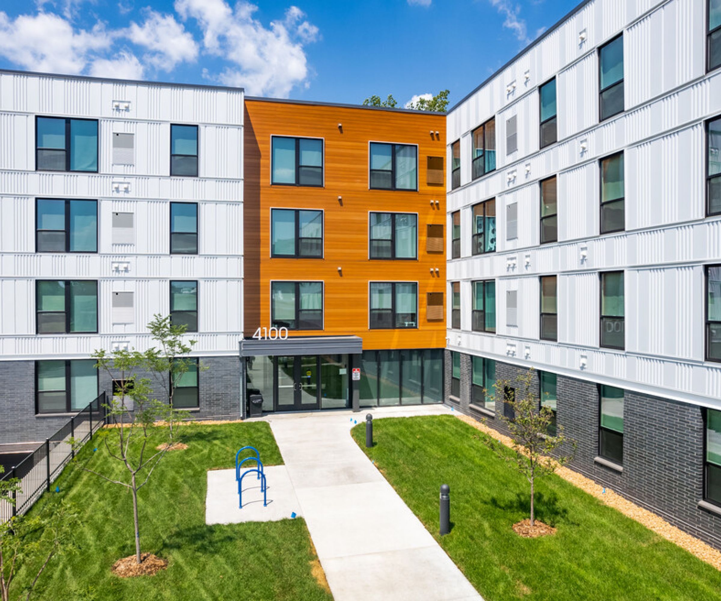 Aeon Affordable Homes and Community Modern, multi-story building with a brick and metal facade, green lawn, playground in front, offering affordable apartment homes.