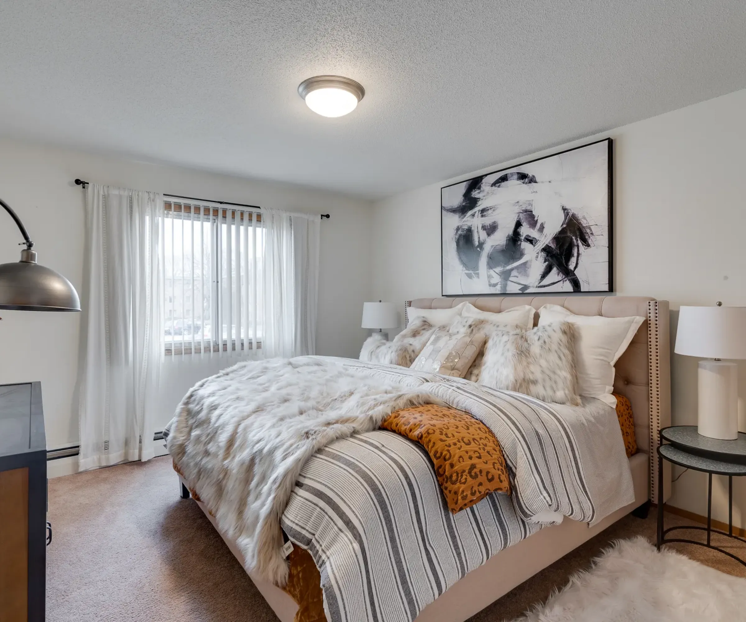 Aeon Affordable Homes Cozy bedroom with a large bed, abstract wall art, fluffy pillows, a throw, and a window with sheer curtains.