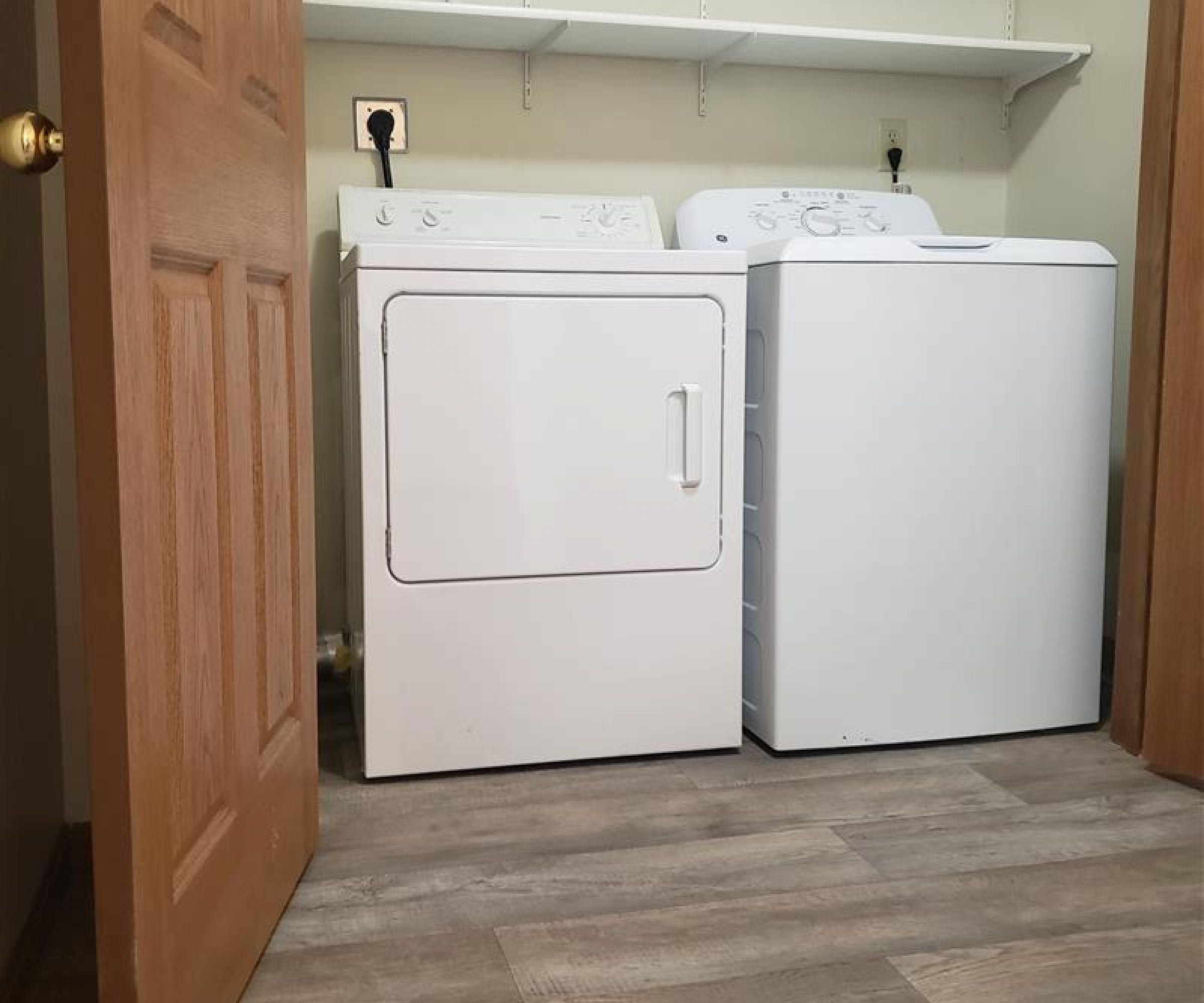 Aeon Affordable Homes and Community Affordable apartment homes featuring a laundry room with a white washer and dryer, wooden floors, an open door, and shelves above.