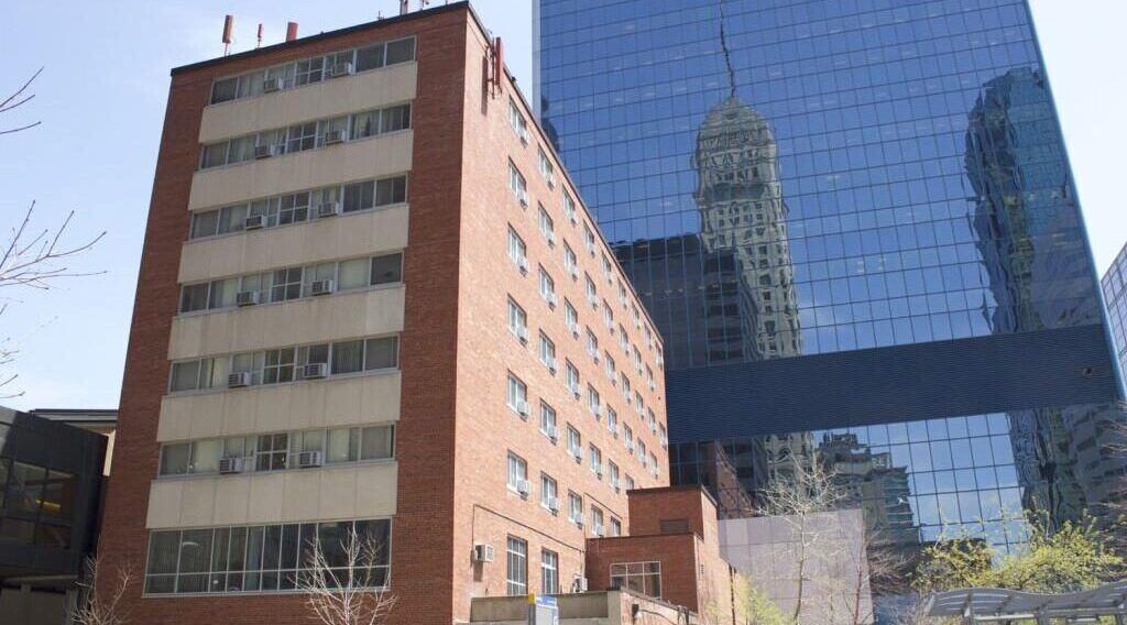 Aeon Affordable Homes A red-brick apartment building stands beside a modern glass skyscraper reflecting the city skyline.