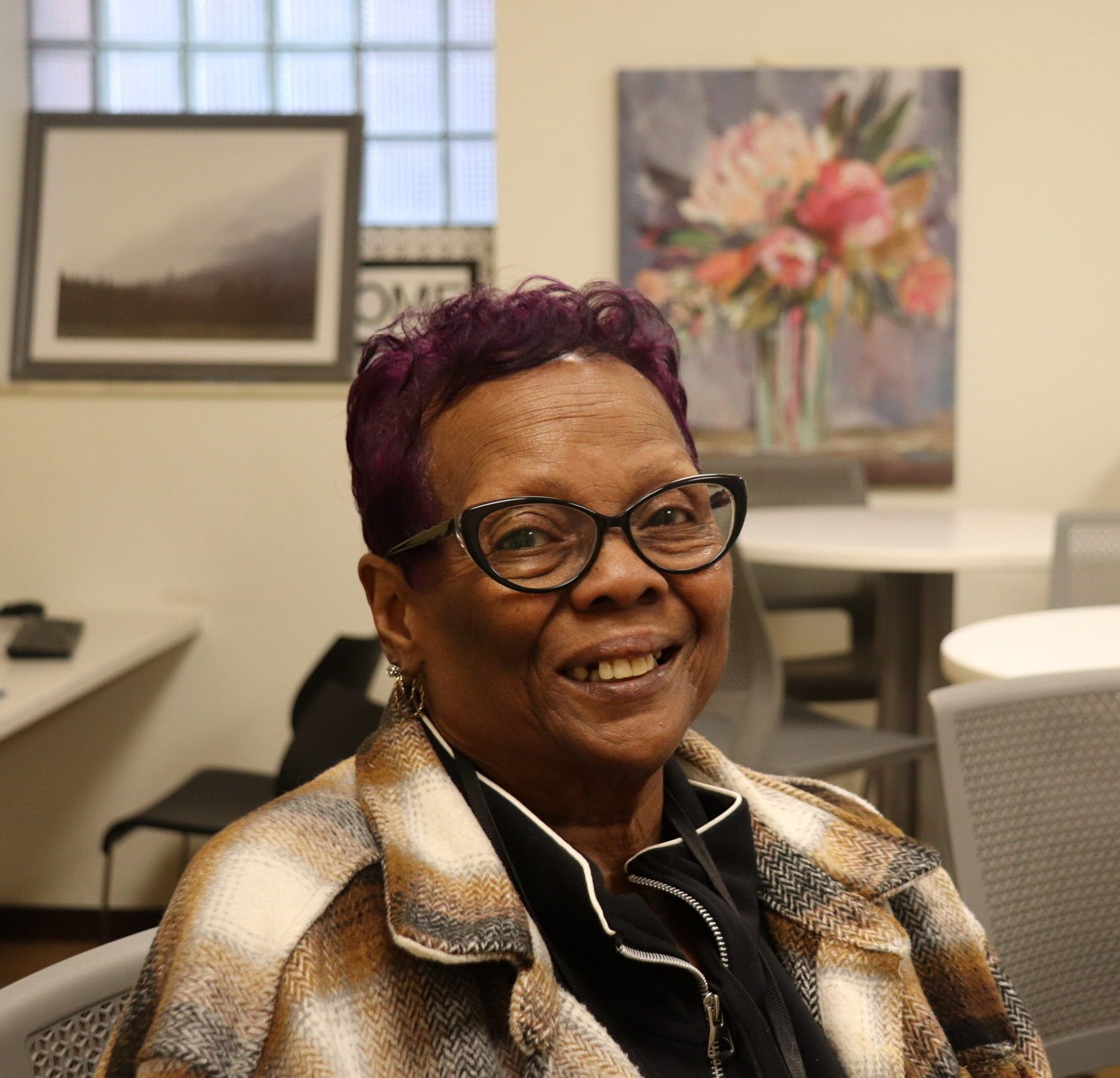 Aeon Affordable Homes Smiling woman with glasses sitting in a room with art on the walls and computers in the background.