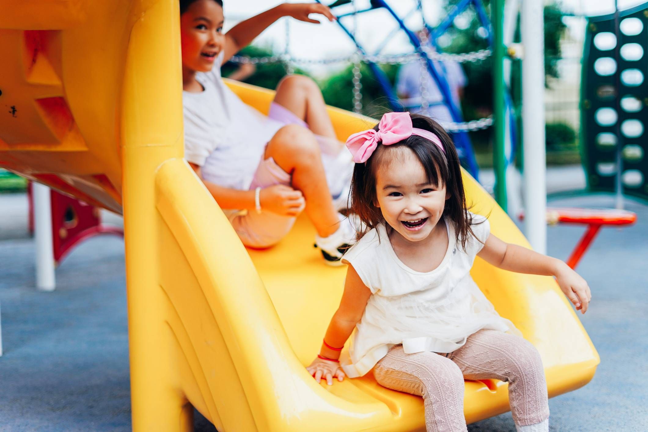 Aeon Affordable Homes Two children smiling, with one sitting on a yellow slide and another above, at a playground.