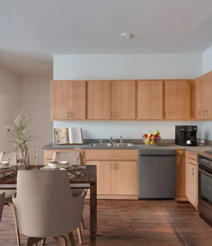 Aeon Affordable Homes and Community Modern kitchen in affordable apartment homes with wooden cabinets, stainless steel appliances, dining table with chairs, and counter decor.