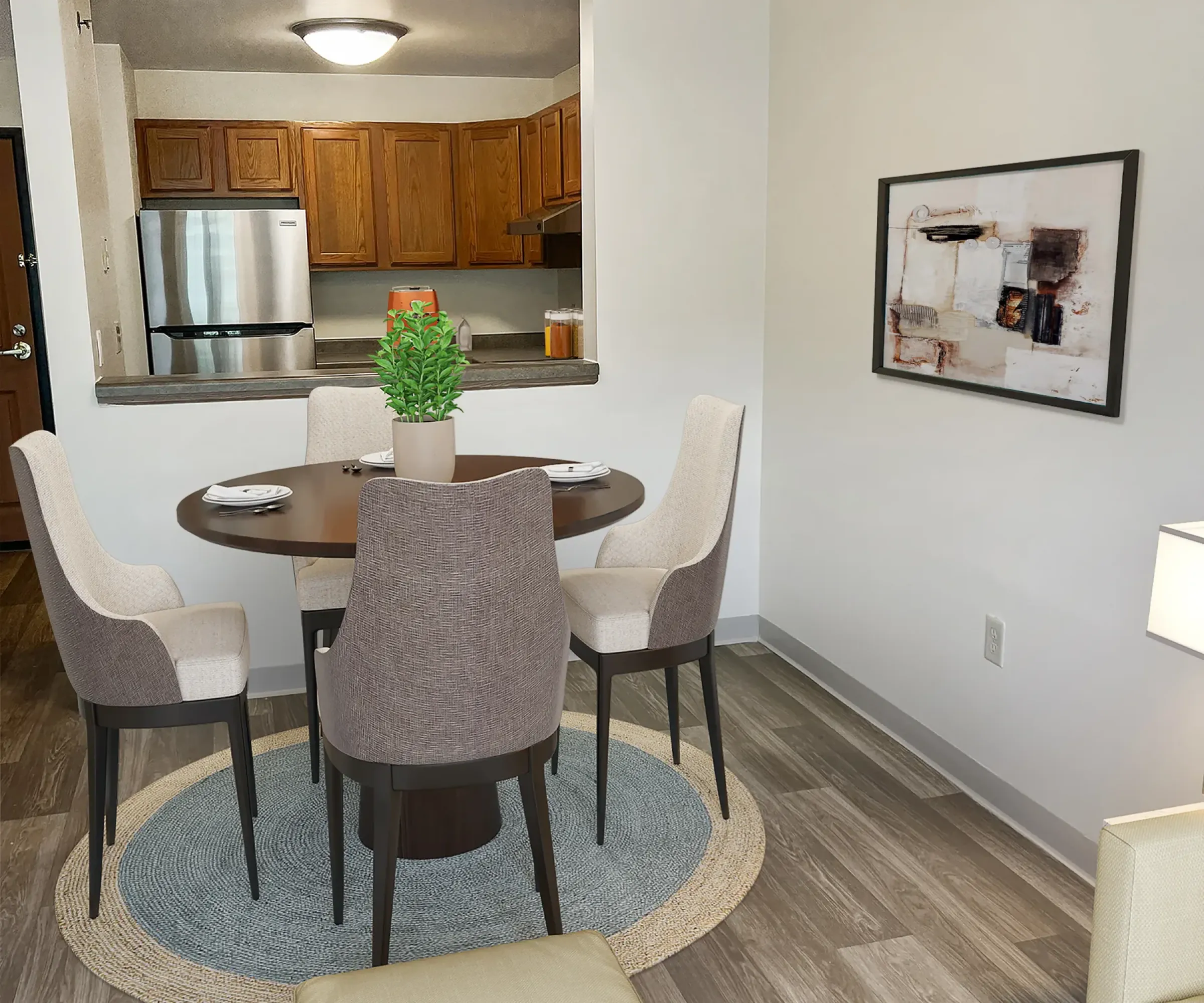 Aeon Affordable Homes and Community Modern dining area in affordable apartment homes with a round table, four chairs, and a plant centerpiece. Background includes a kitchen and artwork.