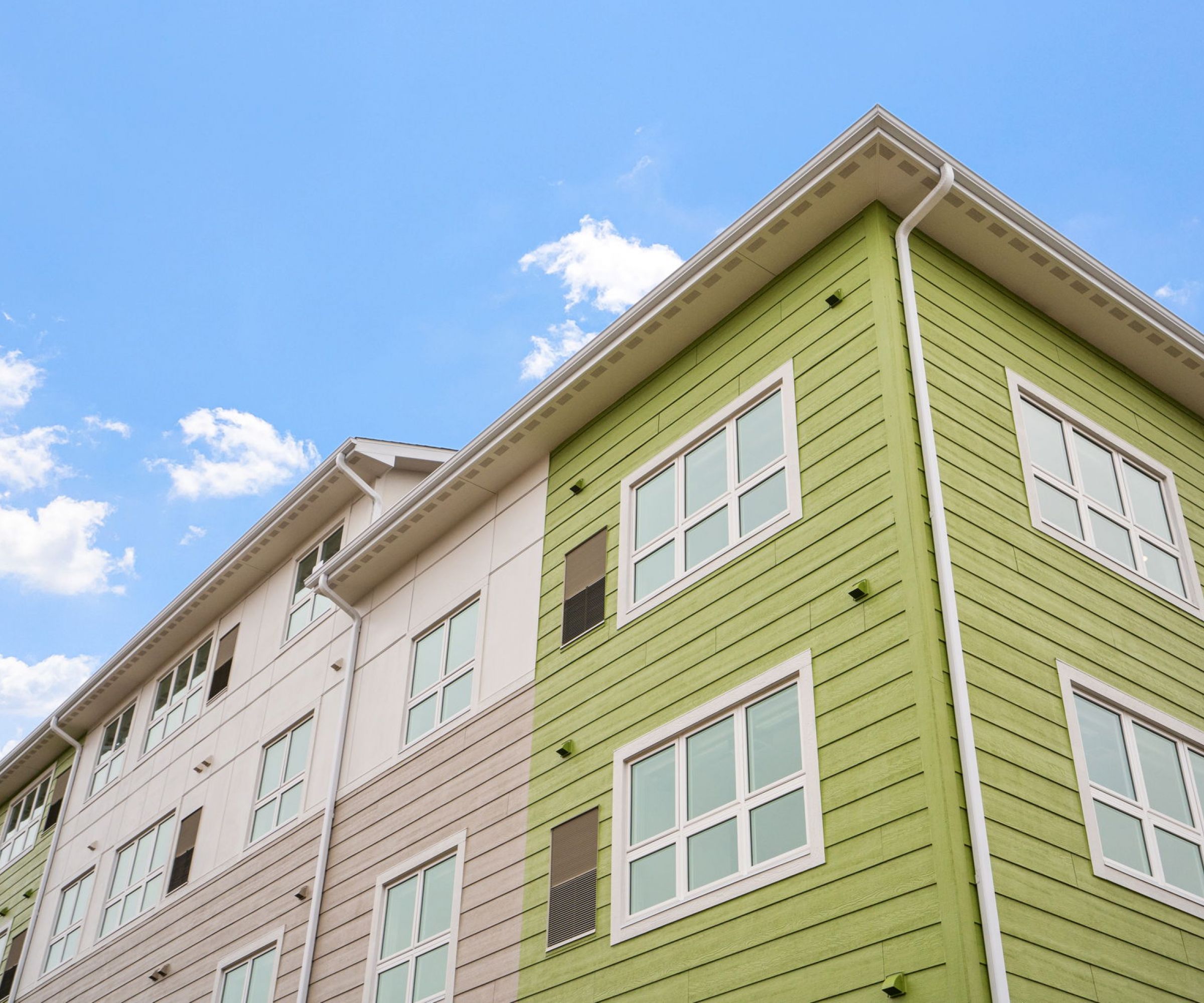 Aeon Affordable Homes and Community Angle view of affordable apartment homes with green and white siding against a blue sky with clouds.
