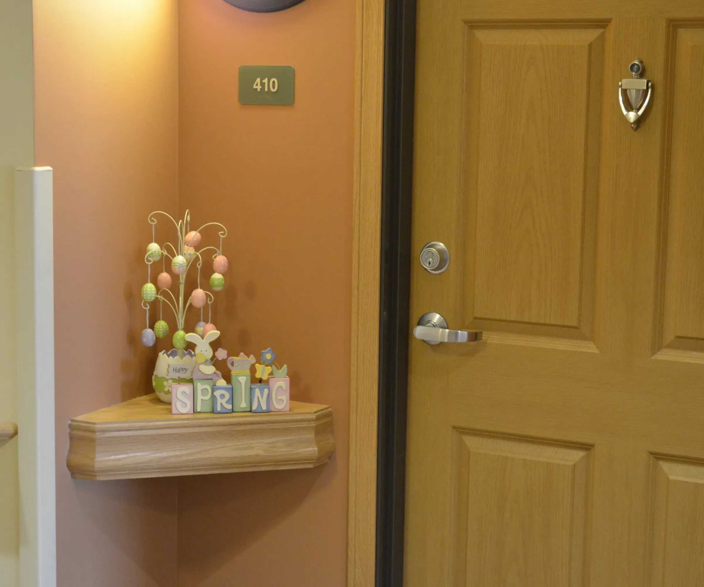 Aeon Affordable Homes and Community Decorative shelf near door with number 410, featuring spring-themed ornaments and a pastel egg tree in affordable apartment homes.