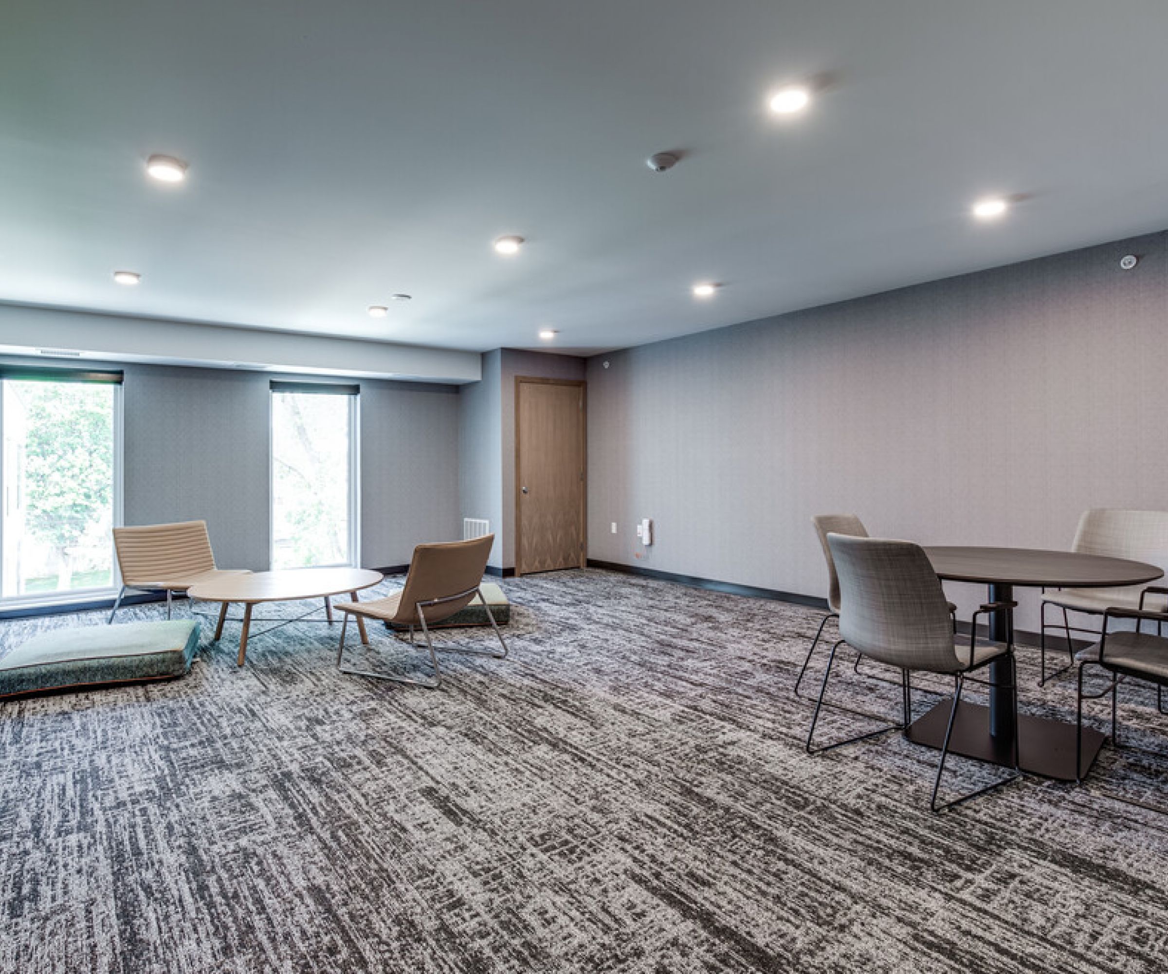 Aeon Affordable Homes and Community Minimalist meeting room with round tables, chairs, large windows, carpeted floor, and soft lighting—perfect for affordable apartment homes.