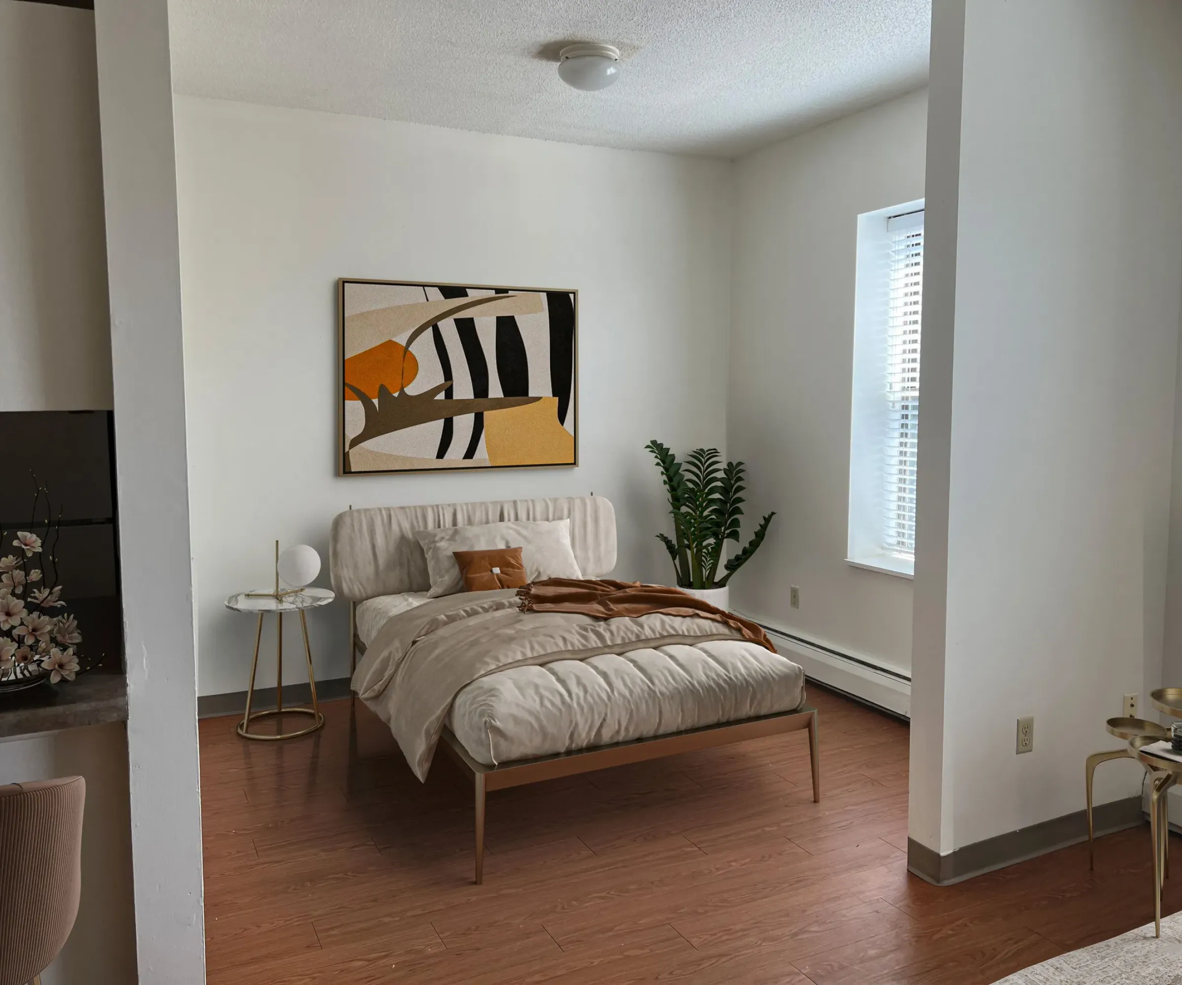 Aeon Affordable Homes and Community Minimalist bedroom in affordable apartment homes, featuring a bed, abstract art, and a potted plant. Light pours in through a window on the right.