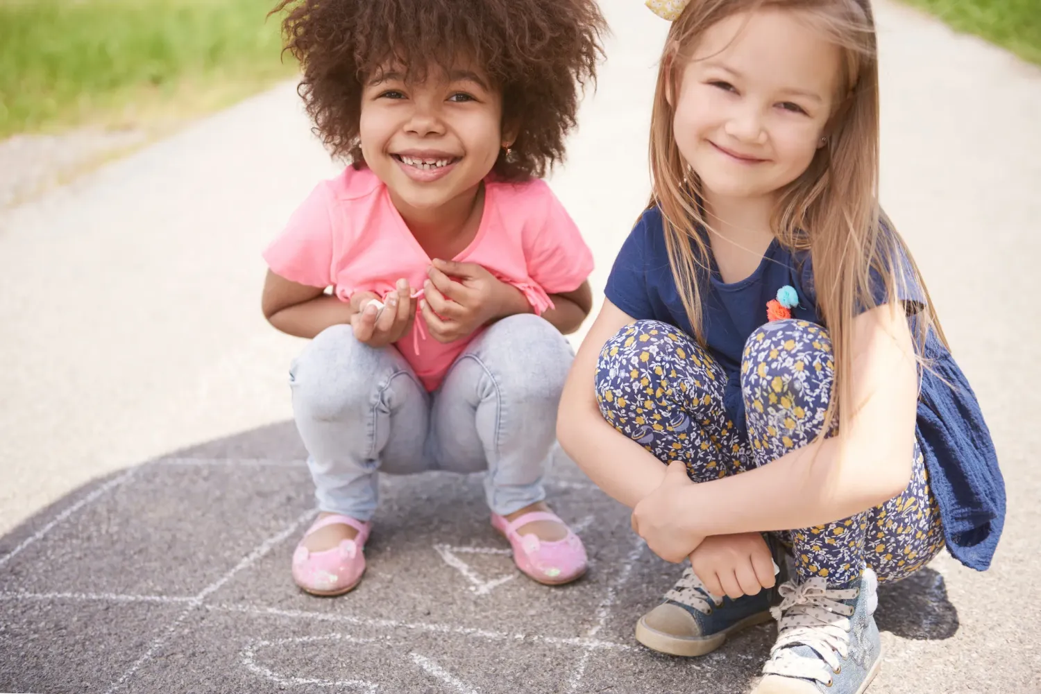 Aeon Affordable Homes with two young girls happily crouching on a sidewalk with chalk drawings. One wears pink, the other blue floral leggings.