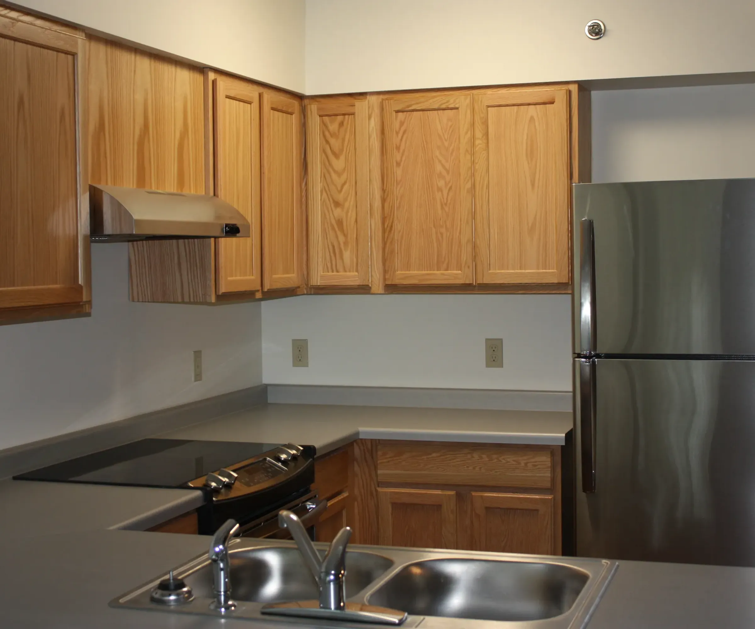 Aeon Affordable Homes and Community Modern kitchen in affordable apartment homes featuring wooden cabinets, electric stovetop, stainless steel refrigerator, and chrome faucet sink.