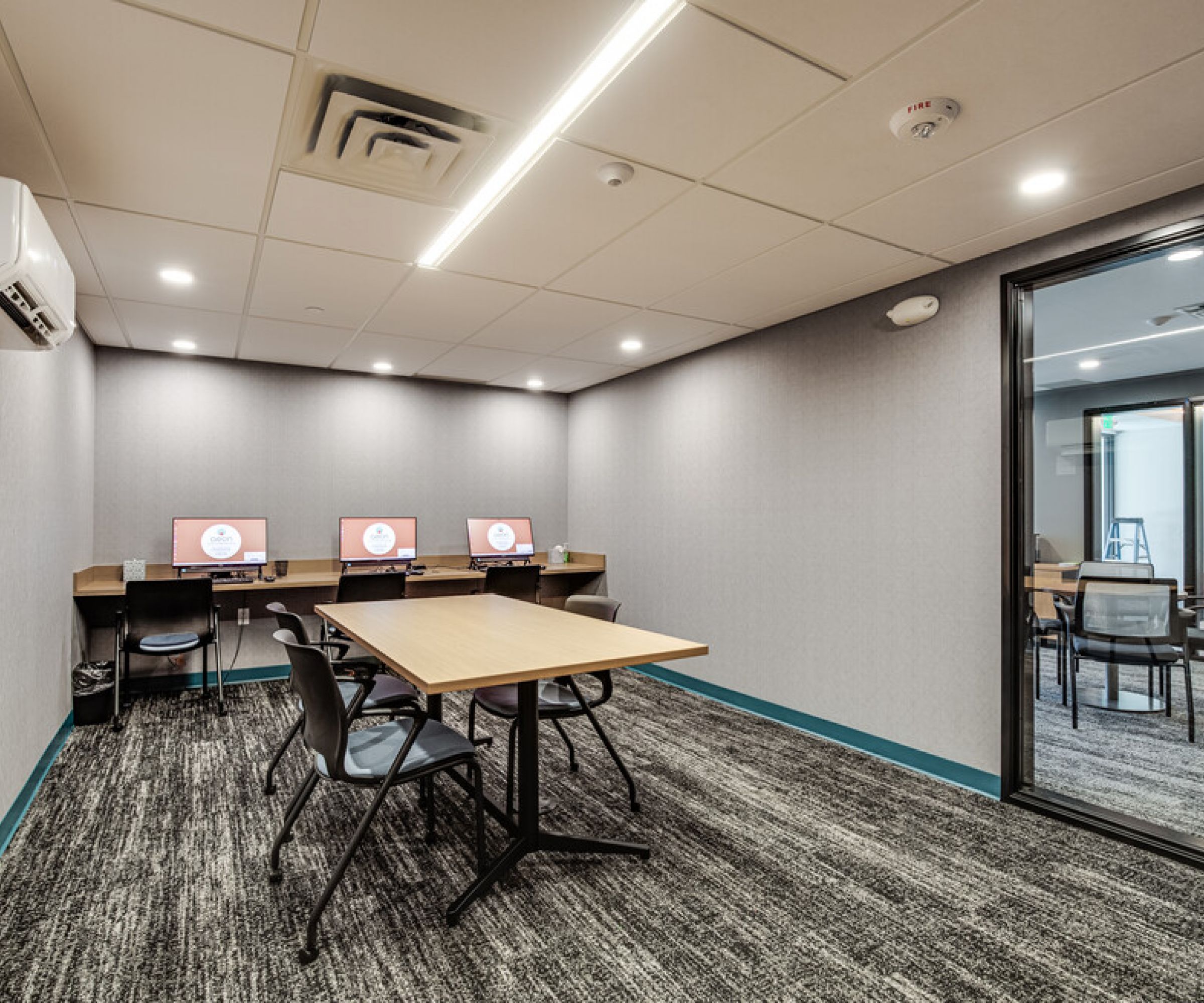 Aeon Affordable Homes and Community Modern conference room in affordable apartment homes with a rectangular table, chairs, and computers on a side counter.