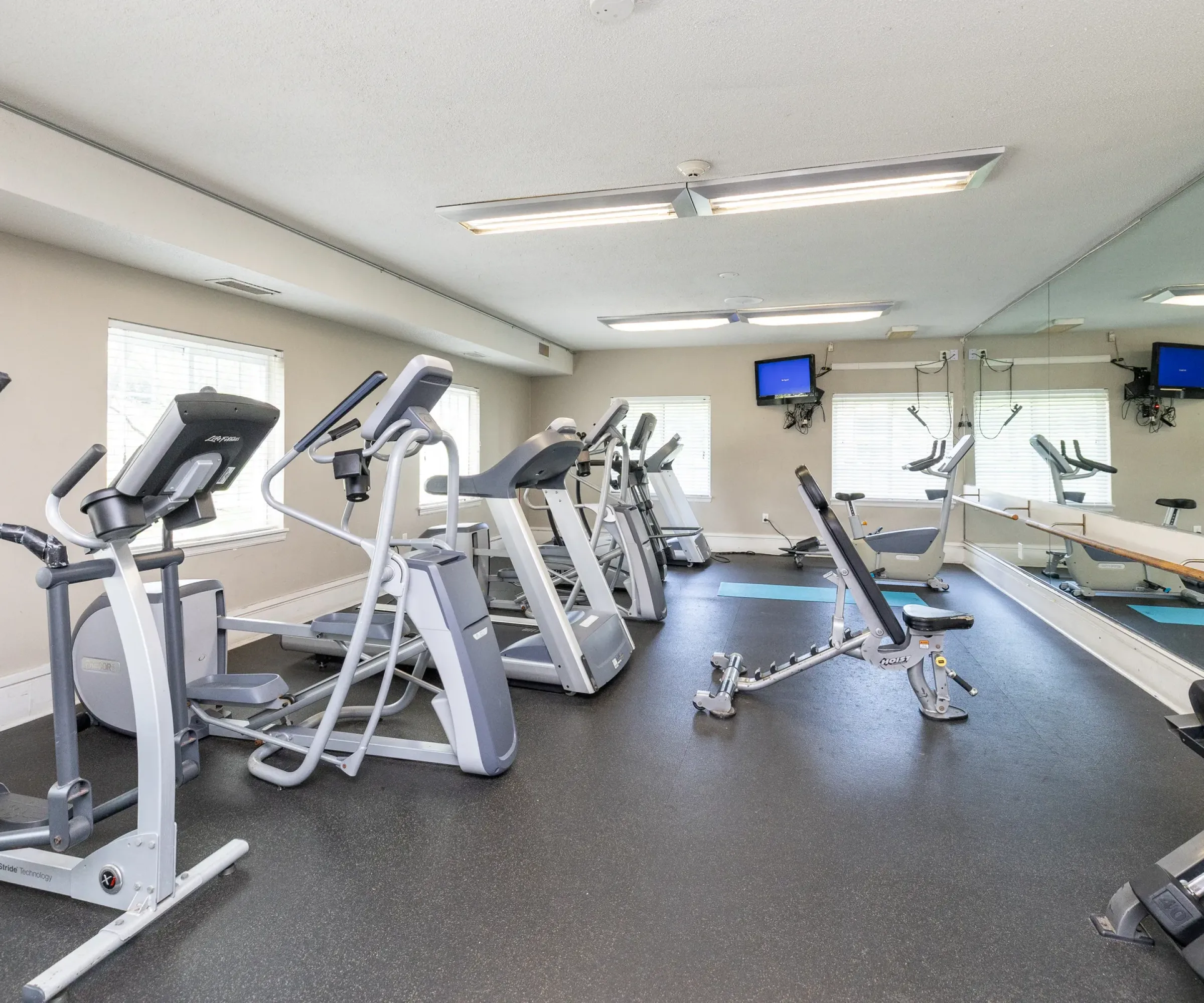 Aeon Affordable Homes A gym with exercise machines, free weights, and a mirrored wall under the bright lights of Blooming Meadows.