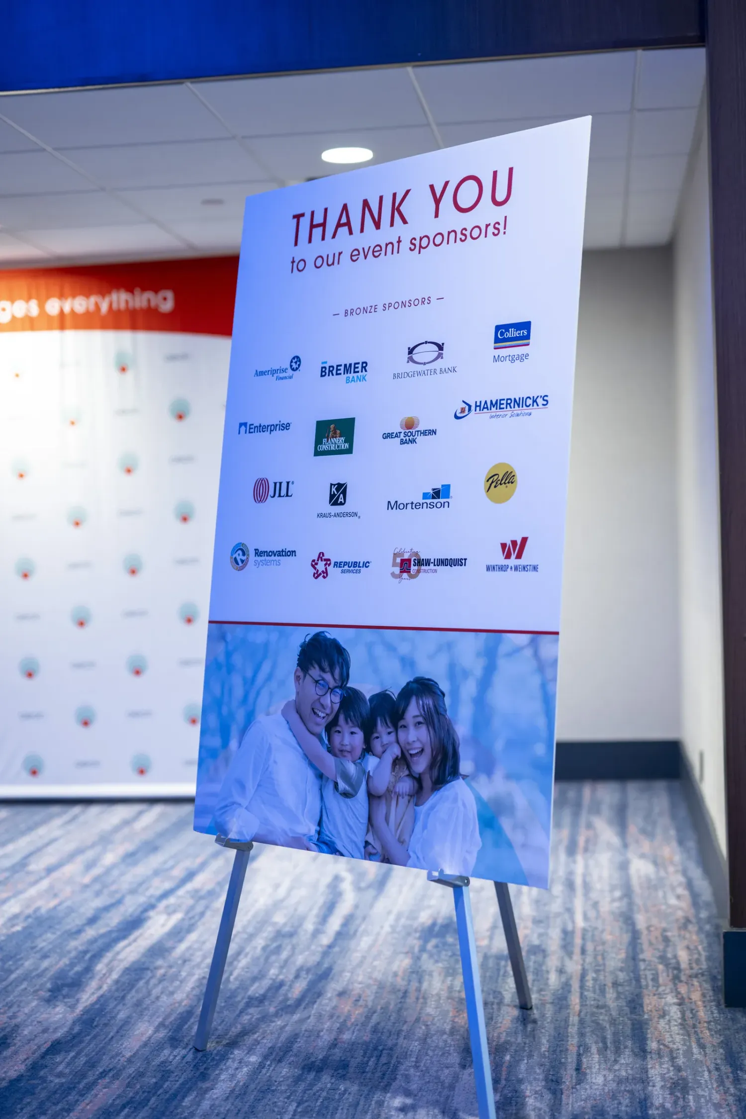 Aeon Affordable Homes Event sponsor sign on an easel, featuring logos and a family photo at the bottom.
