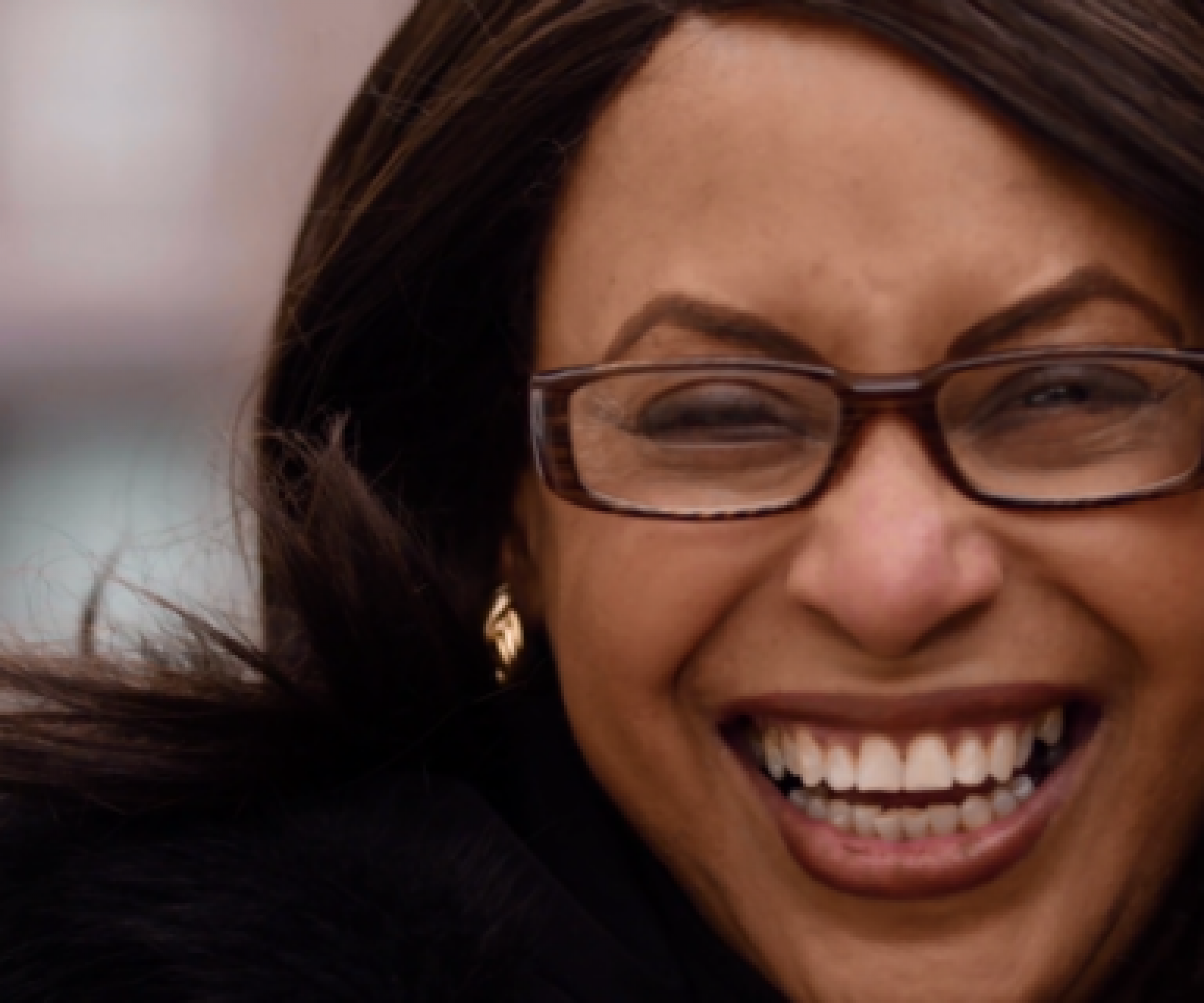 Aeon Affordable Homes and Community A person with glasses smiling brightly and wearing a black coat.