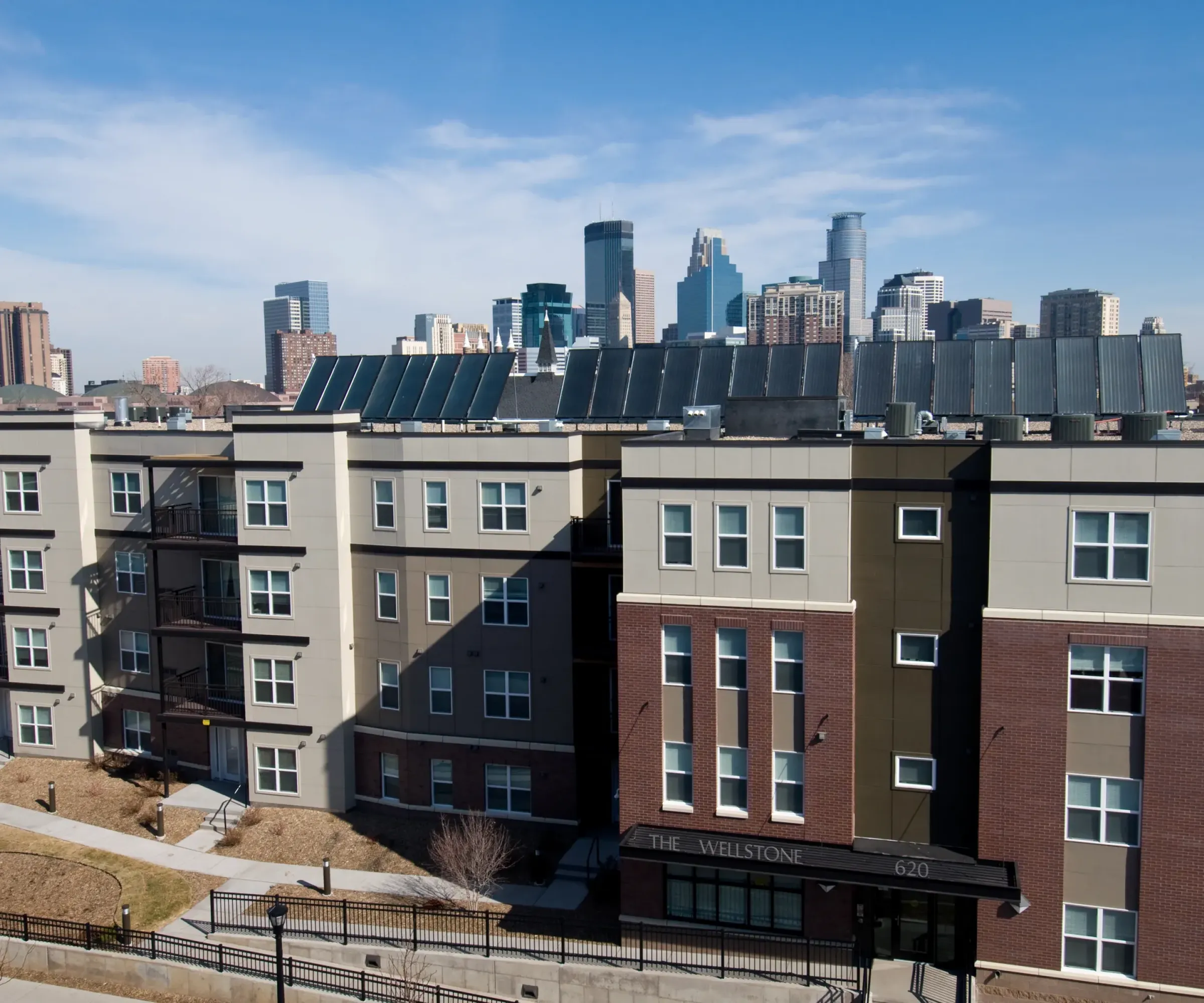 Aeon Affordable Homes and Community Affordable apartment homes with balconies and solar panels overlook a city skyline on a clear day.