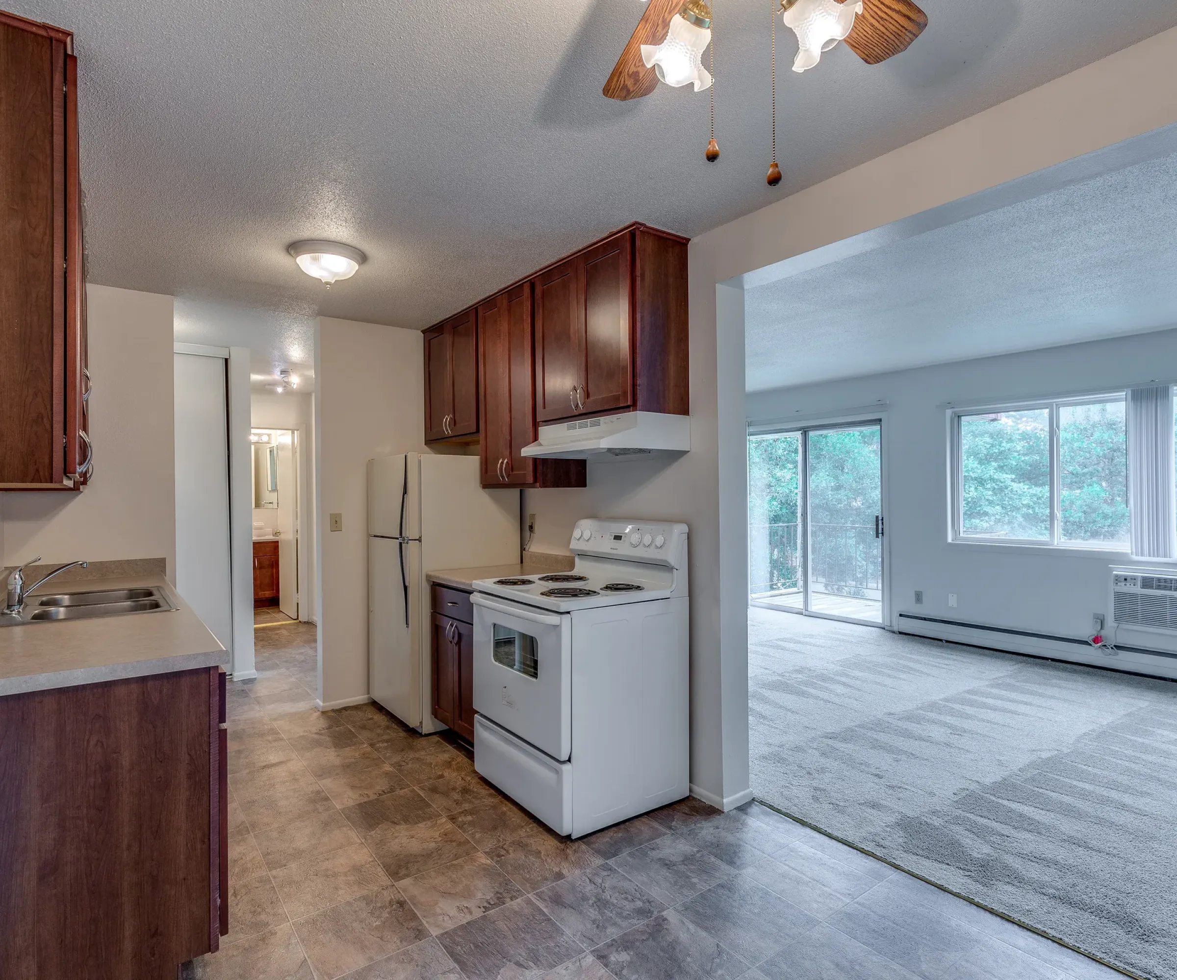 Aeon Affordable Homes Seasons Park Apartments unit interior with kitchen, living room, and sliding door to balcony with trees