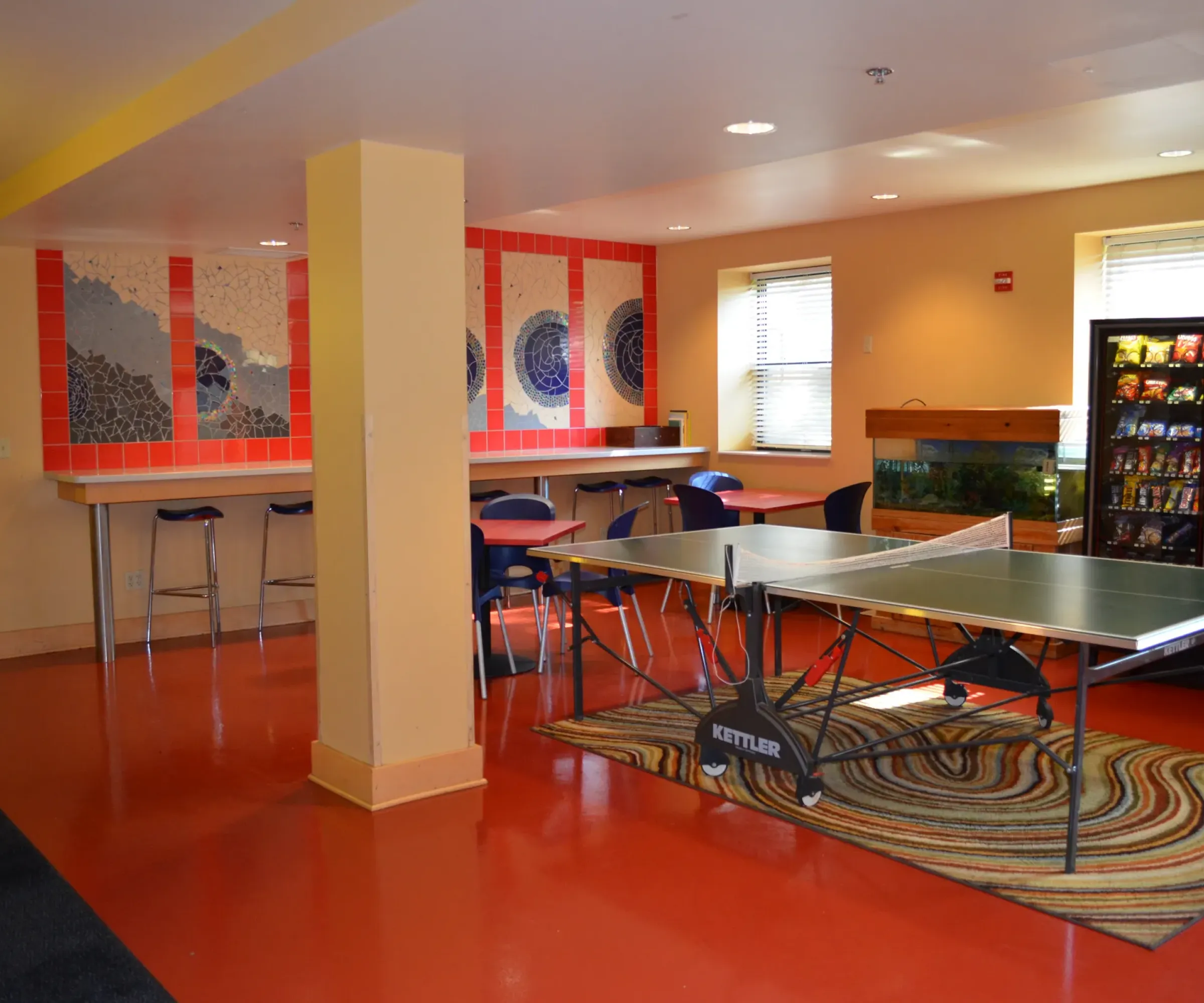 Aeon Affordable Homes and Community A recreation room in our affordable apartment homes features a ping pong table, bar-style seating, vending machines, and colorful wall art.