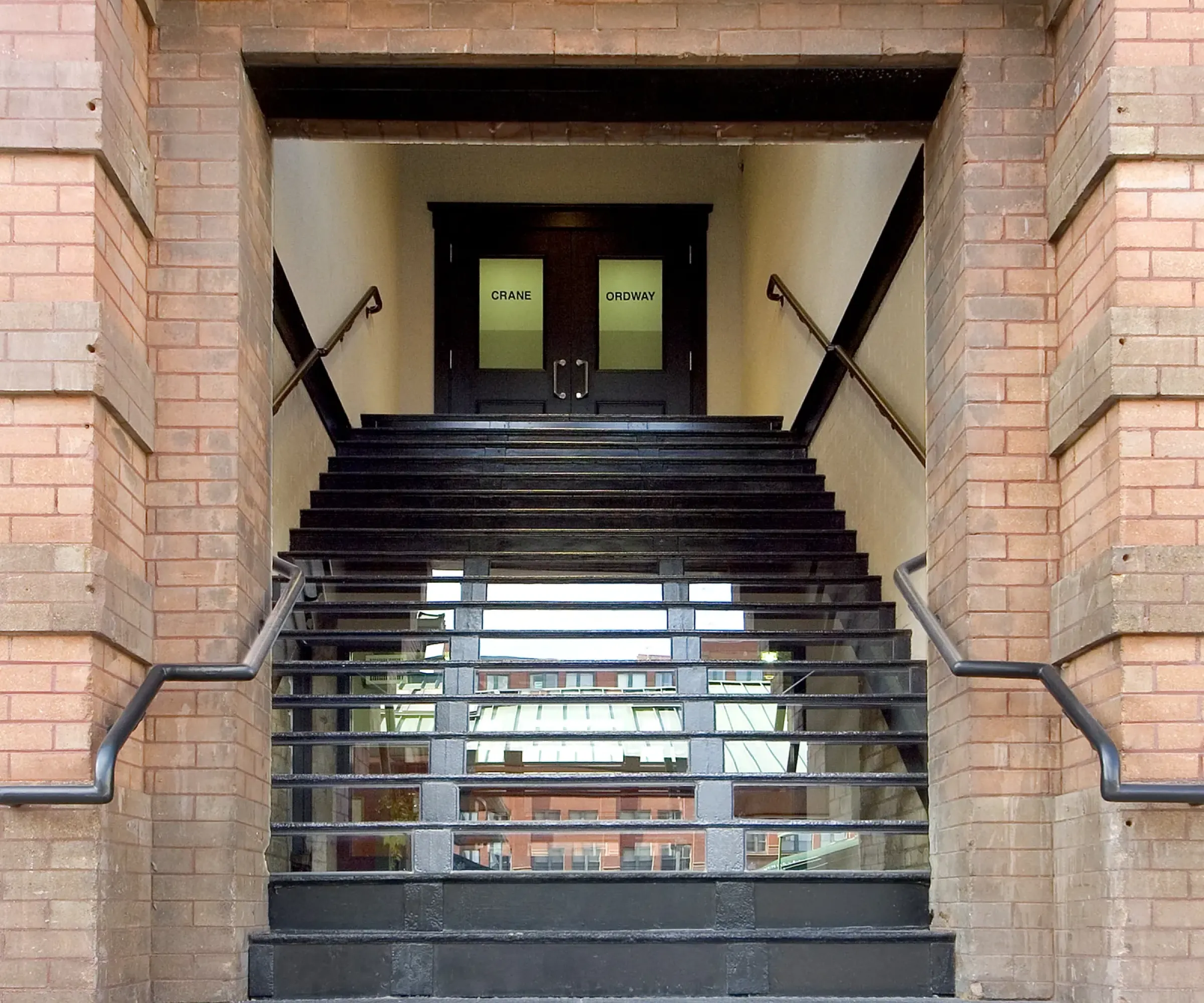 Aeon Affordable Homes and Community Brick building entrance with black stairs leading to glass doors labeled "CRAIG" and "OPERA," offering affordable apartment homes.