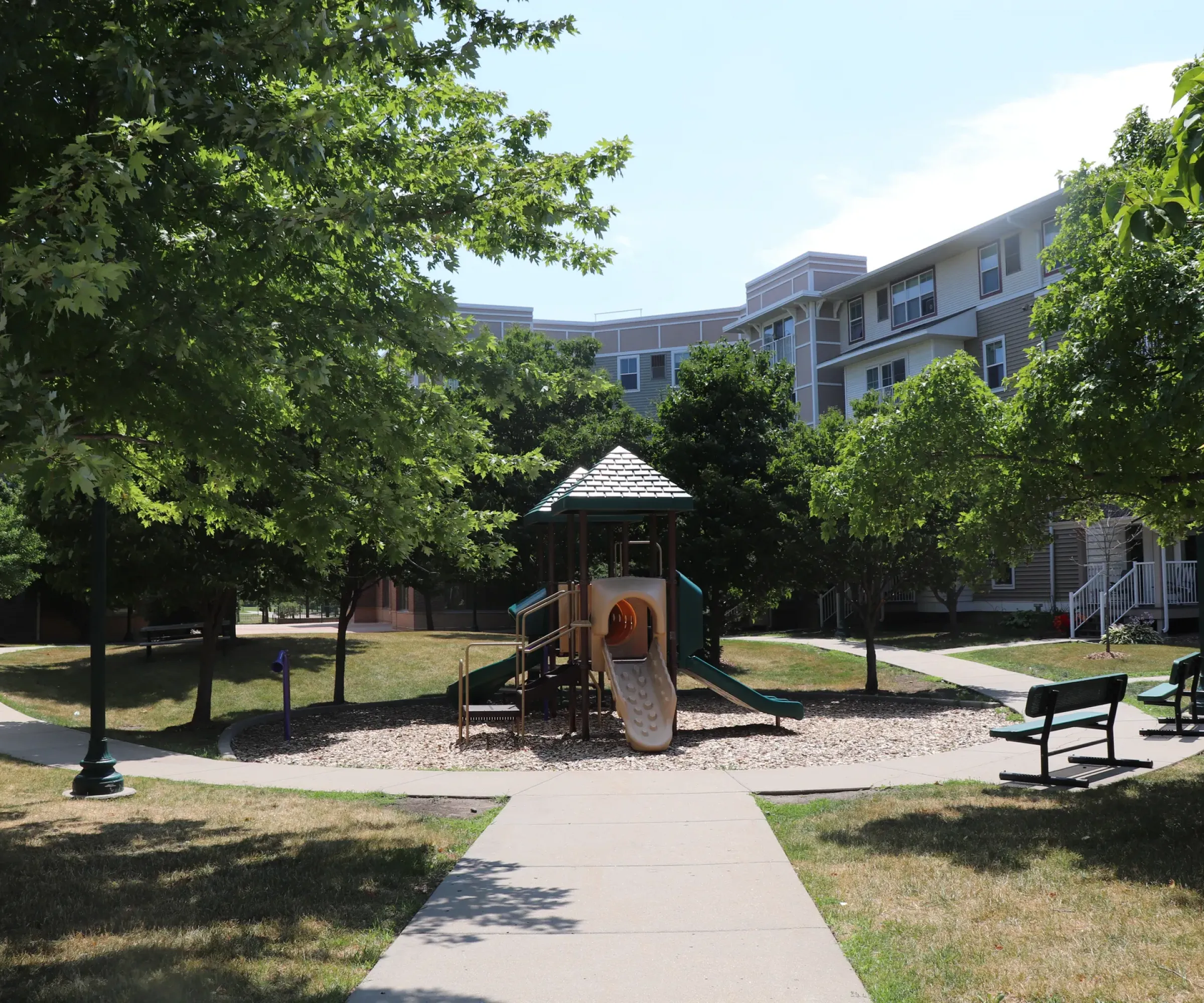 Aeon Affordable Homes and Community Playground with a slide and climbing structure, surrounded by trees and benches, near affordable apartment homes.