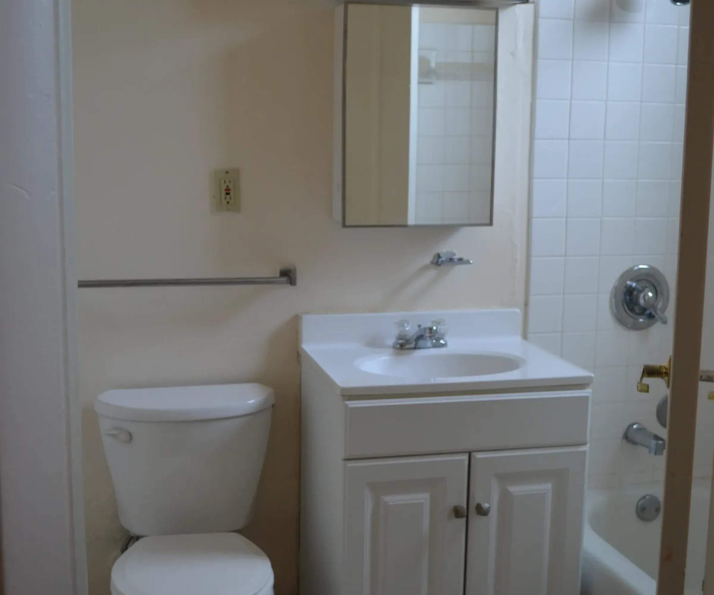 Aeon Affordable Homes and Community Affordable apartment homes featuring a compact bathroom with a toilet, sink, mirrored cabinet, and shower-tub combo. White tiles and fixtures.