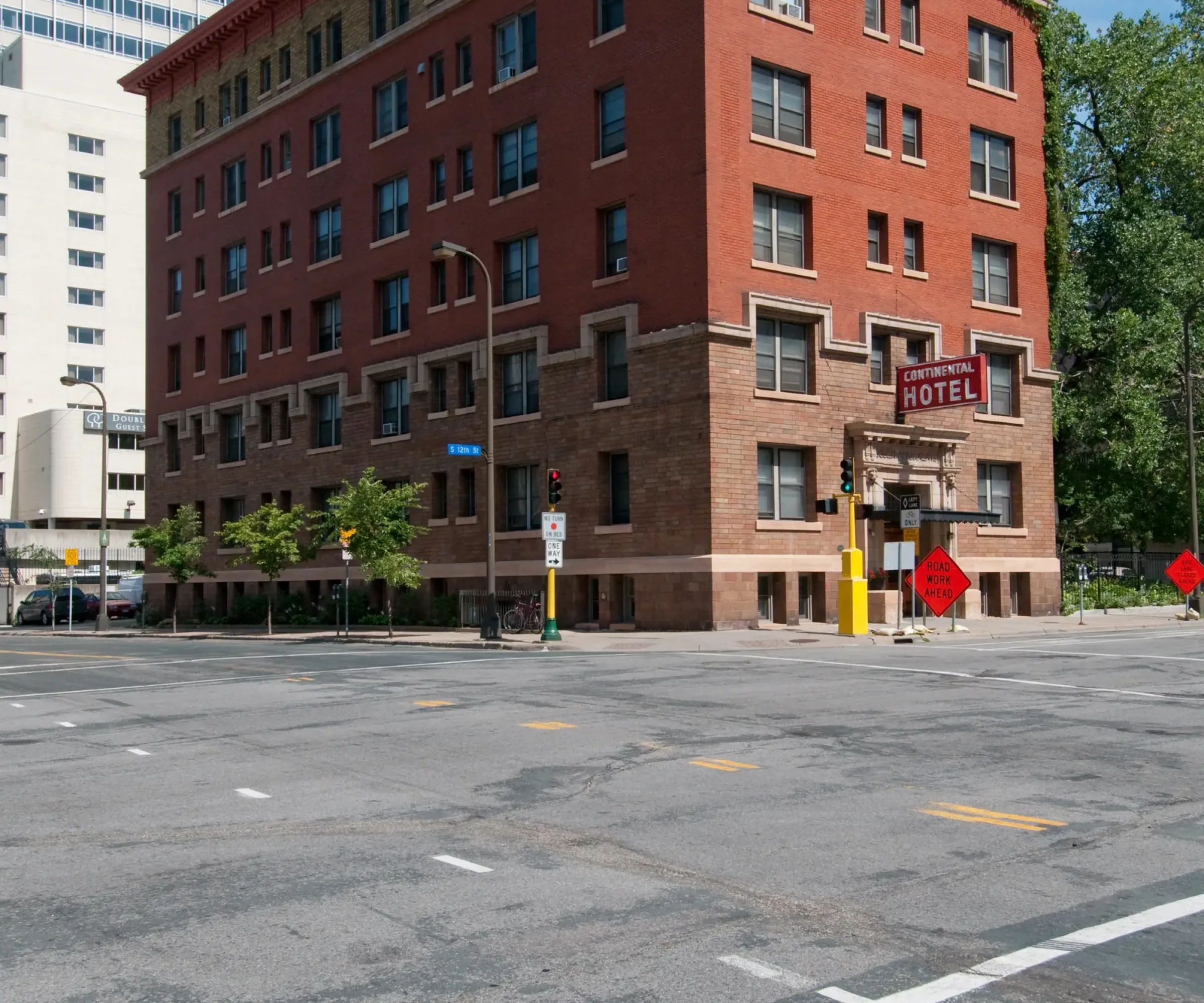 Aeon Affordable Homes and Community Red brick hotel on a city corner, surrounded by trees and skyscrapers, offers views akin to affordable apartment homes under a clear blue sky.