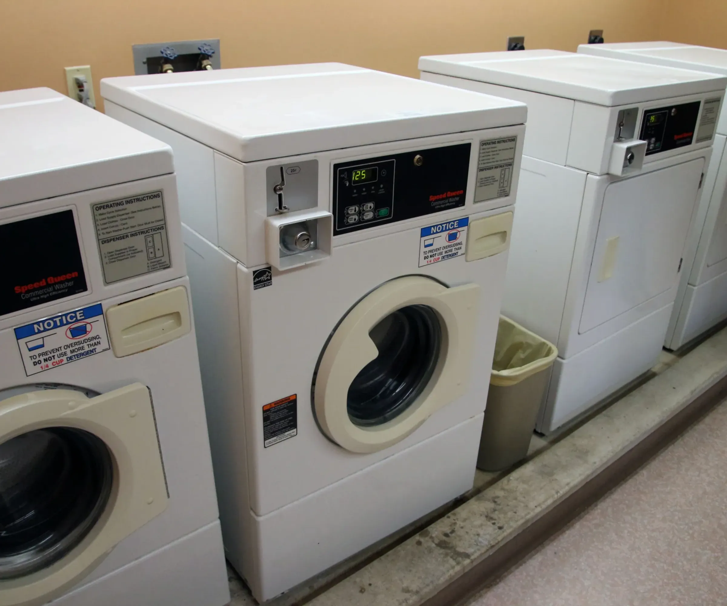 Aeon Affordable Homes and Community Row of commercial washing machines in a laundromat, ideal for residents of nearby affordable apartment homes, each with digital displays and coin slots.