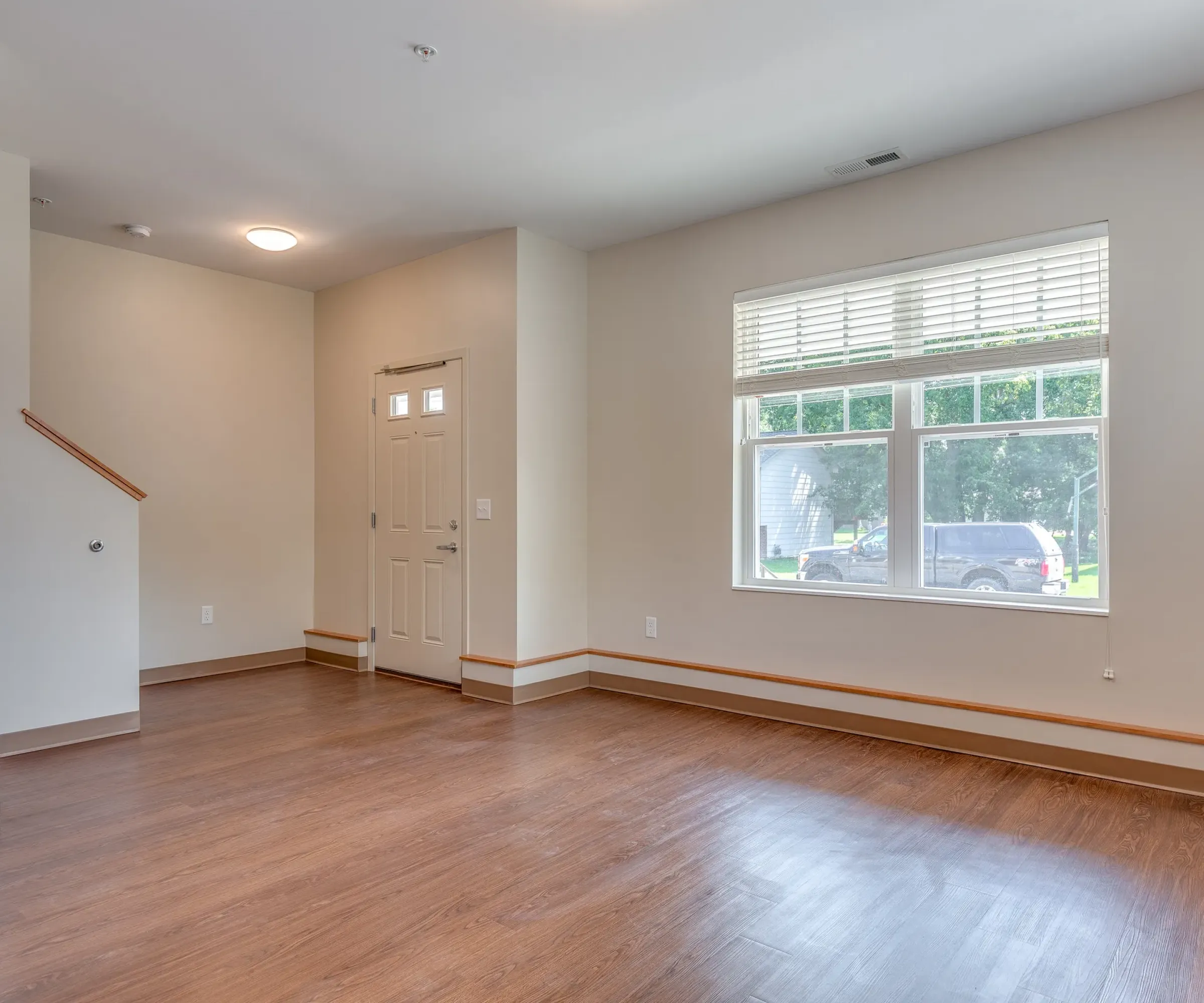Aeon Affordable Homes and Community Bright, affordable apartment home with wooden floors, large window, and beige door. Stairs visible on the left.