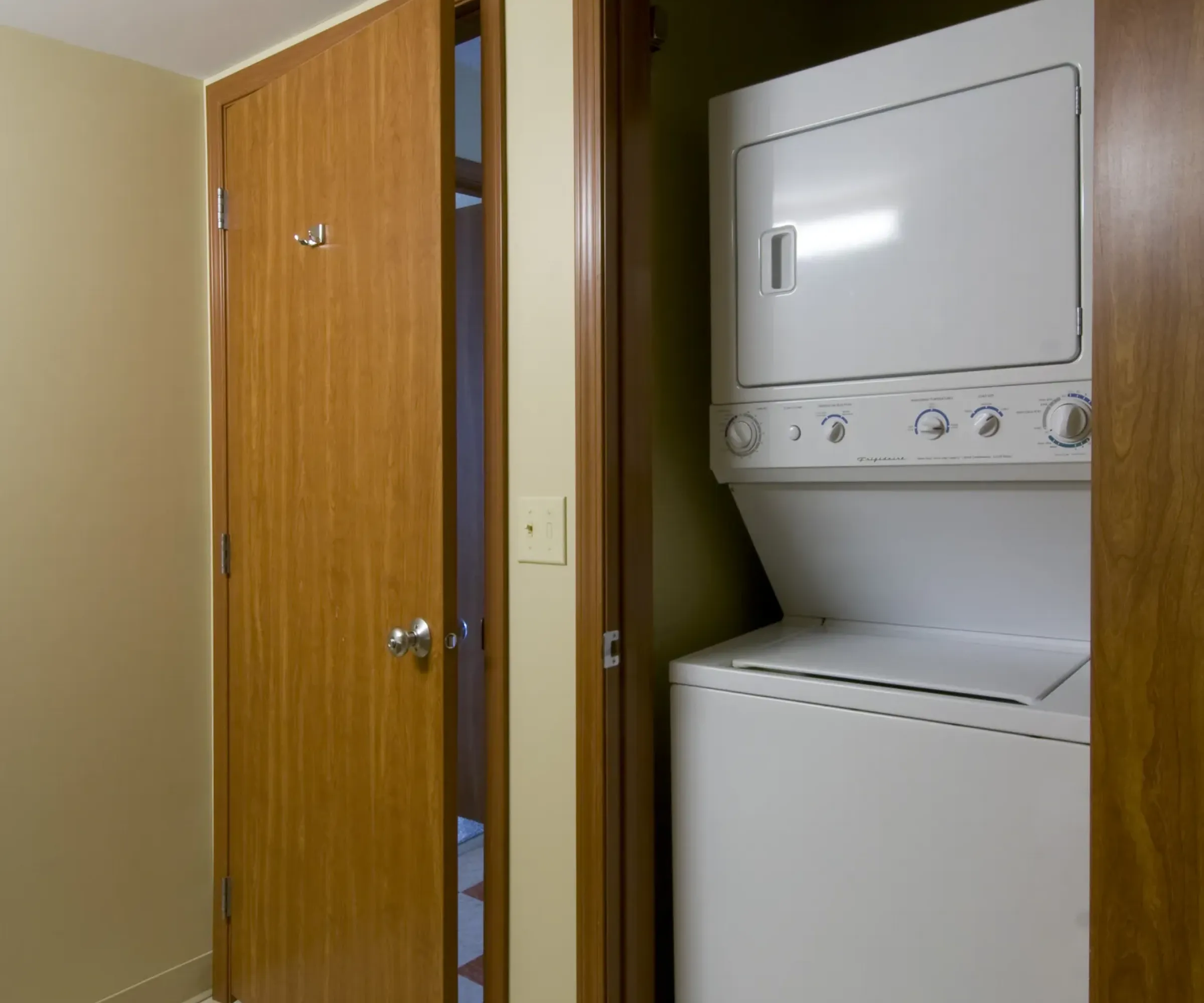 Aeon Affordable Homes and Community Stacked washer and dryer in a small laundry closet with open wooden doors, perfect for affordable apartment homes.