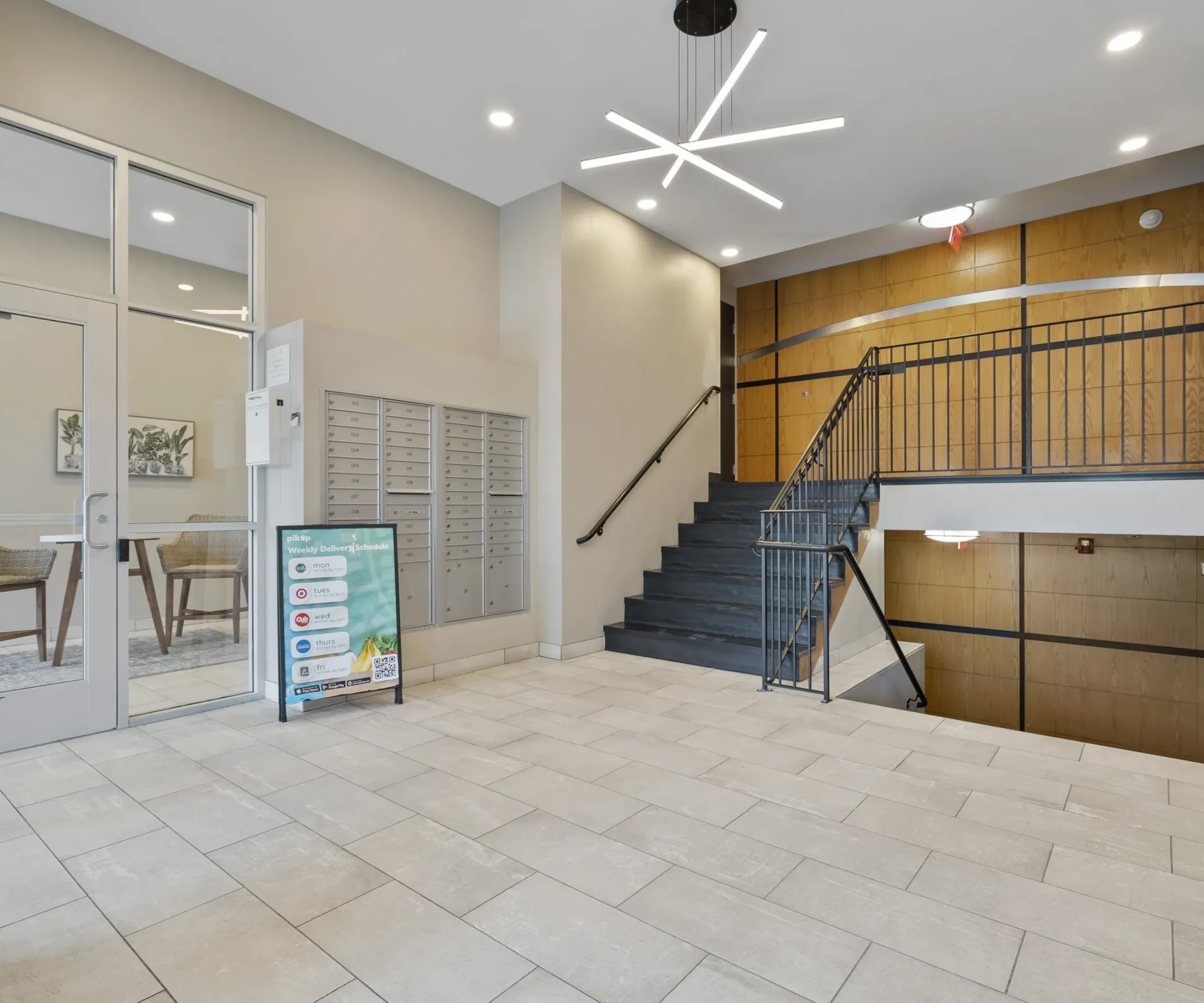 Aeon Affordable Homes Modern lobby with mailboxes, glass doors, a staircase, and a geometric light fixture on the ceiling.