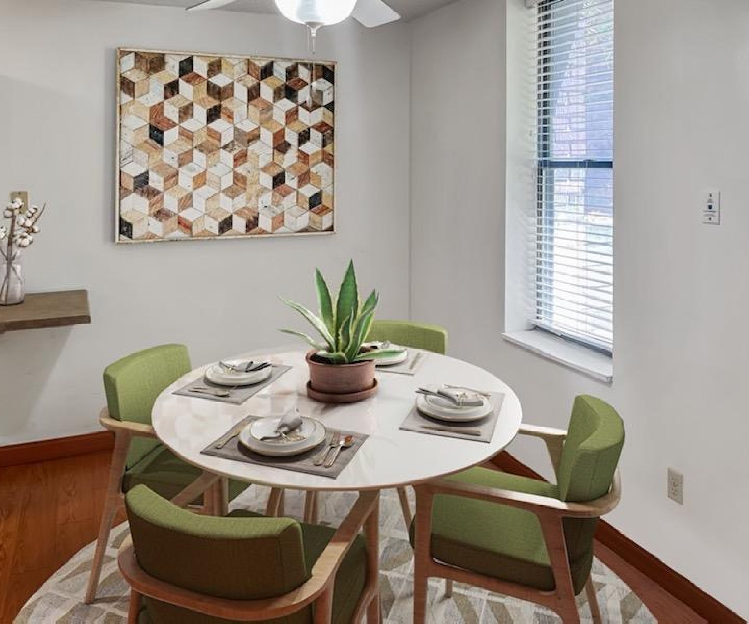 Aeon Affordable Homes and Community Affordable apartment homes featuring a dining room with a round table, green chairs, geometric wall art, and a potted plant in natural light.
